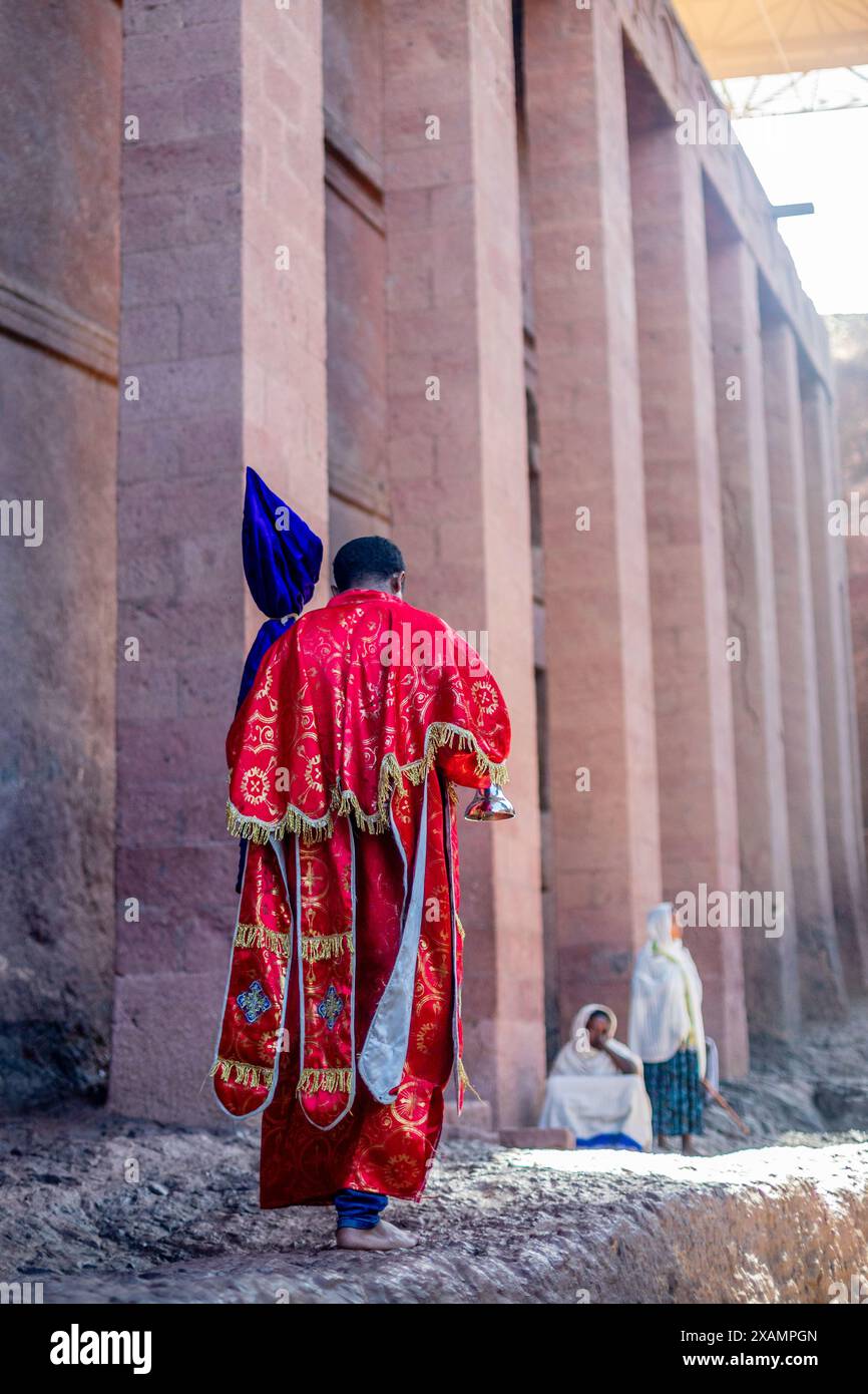Ortodox uomo sacerdote in tessuto rosso che cammina alle pareti della chiesa monolitica ortodox di Bete Medham Alem, Lalibela, regione di Amhara, Etiopia. Foto Stock