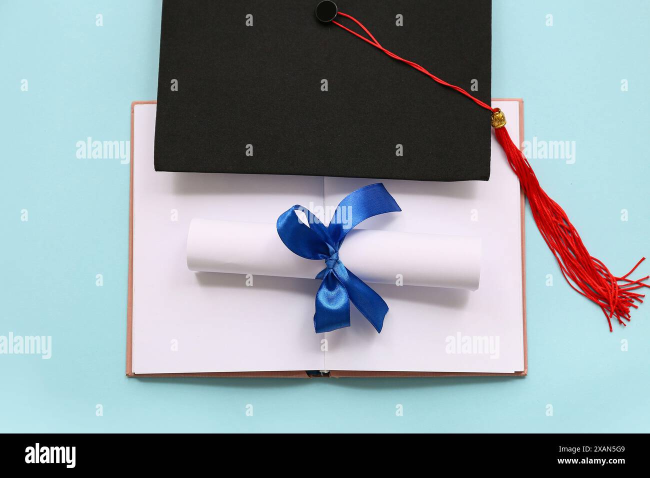 Diploma con nastro blu, libro aperto e cappello graduato su sfondo azzurro Foto Stock