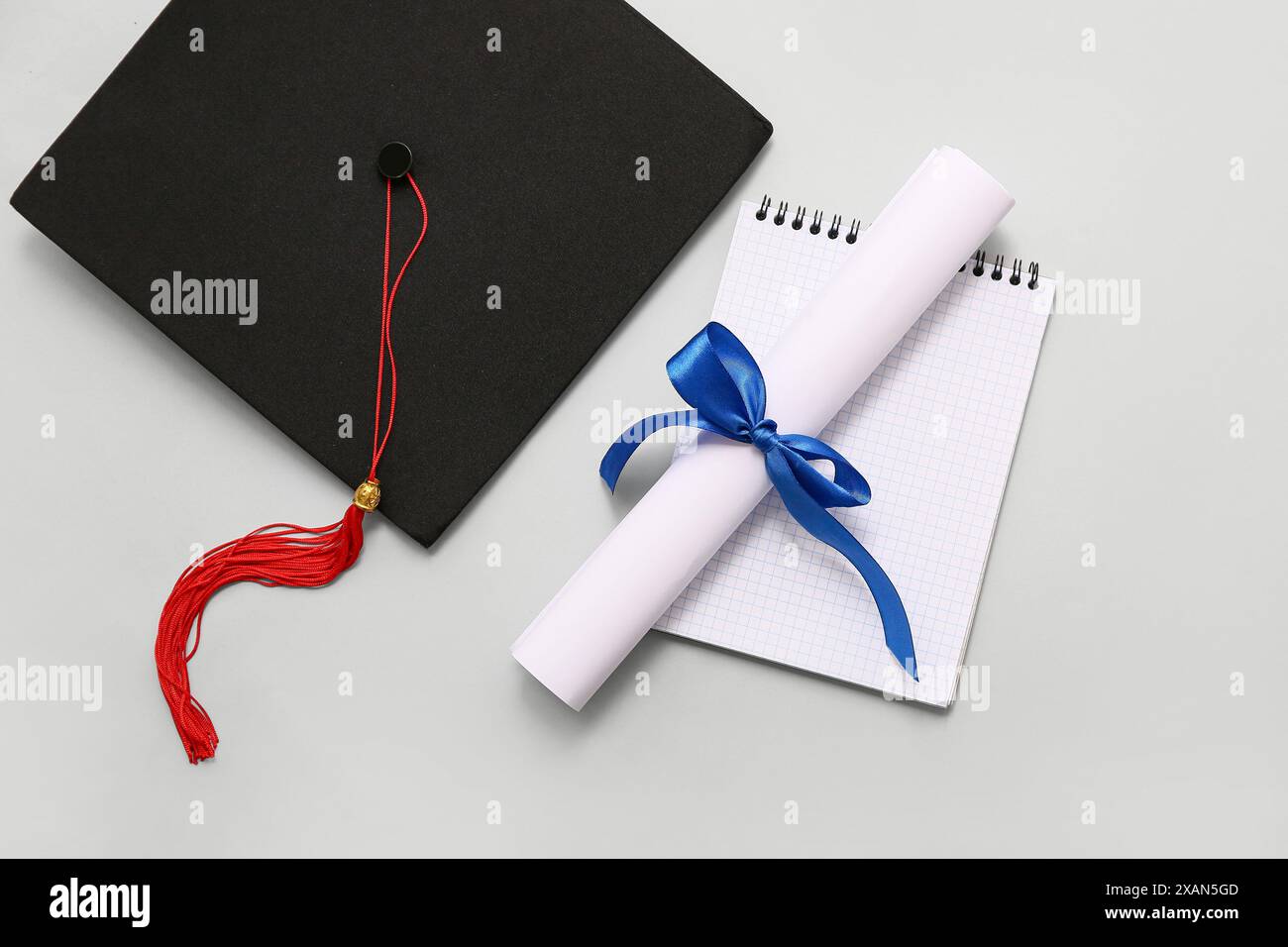 Diploma con nastro blu, libro aperto e cappello graduato su sfondo bianco Foto Stock