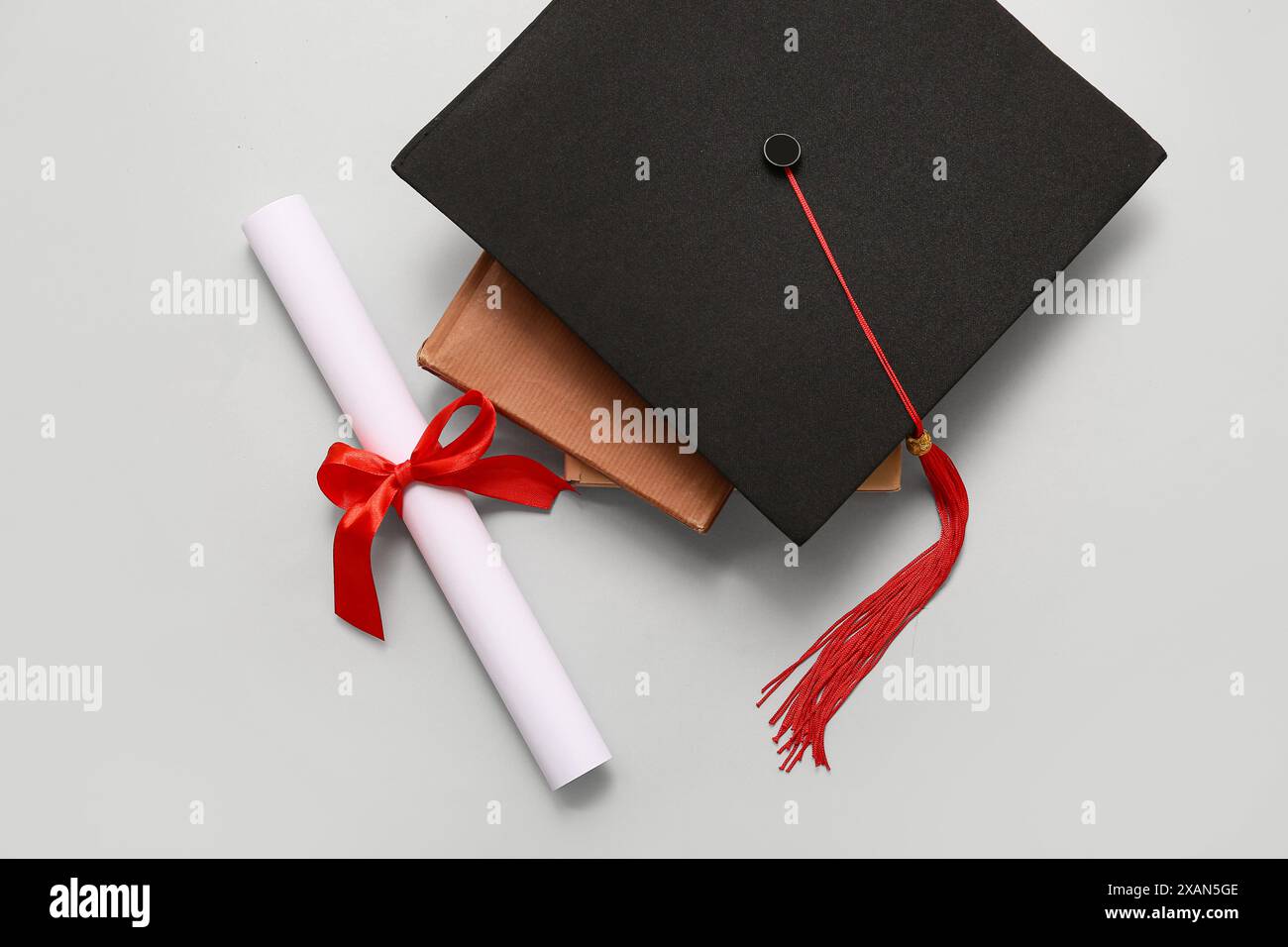Diploma con nastro rosso, libro e cappello graduato su sfondo bianco Foto Stock