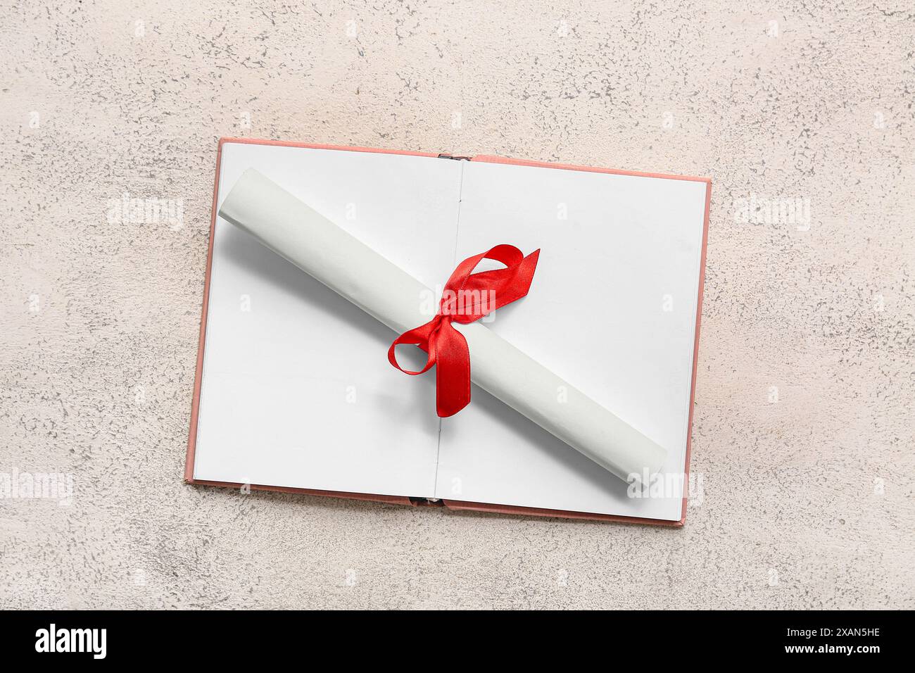Diploma con nastro rosso e libro aperto su sfondo grunge bianco Foto Stock