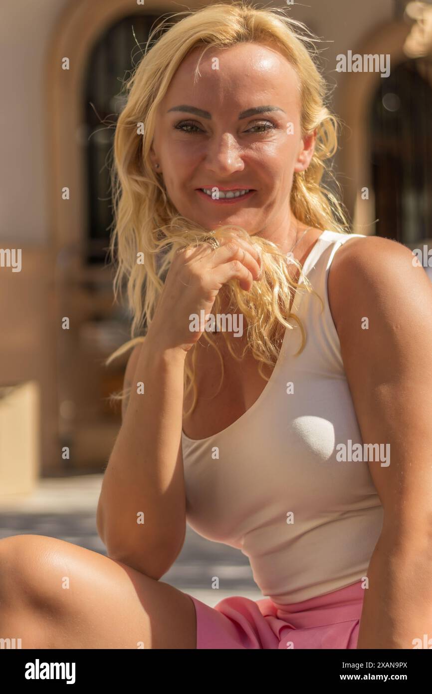 Questa immagine cattura un ritratto ravvicinato di una donna bionda con occhi verdi sorprendenti e il suo sorriso radioso che illumina la cornice. Foto Stock