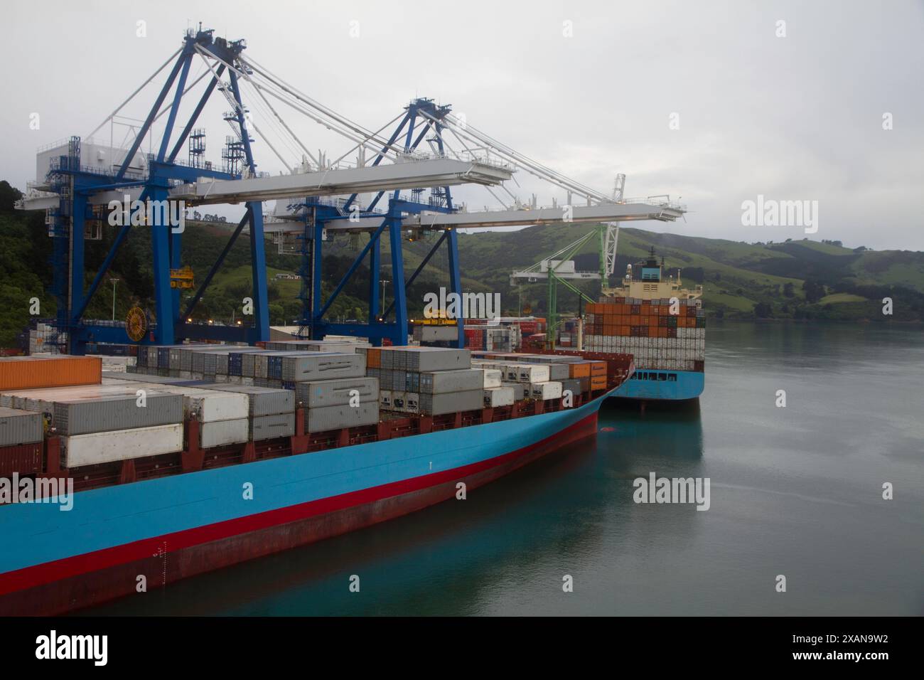Affacciato sui porti con una nave da carico attraccata al porto con montagne verdi sullo sfondo Foto Stock