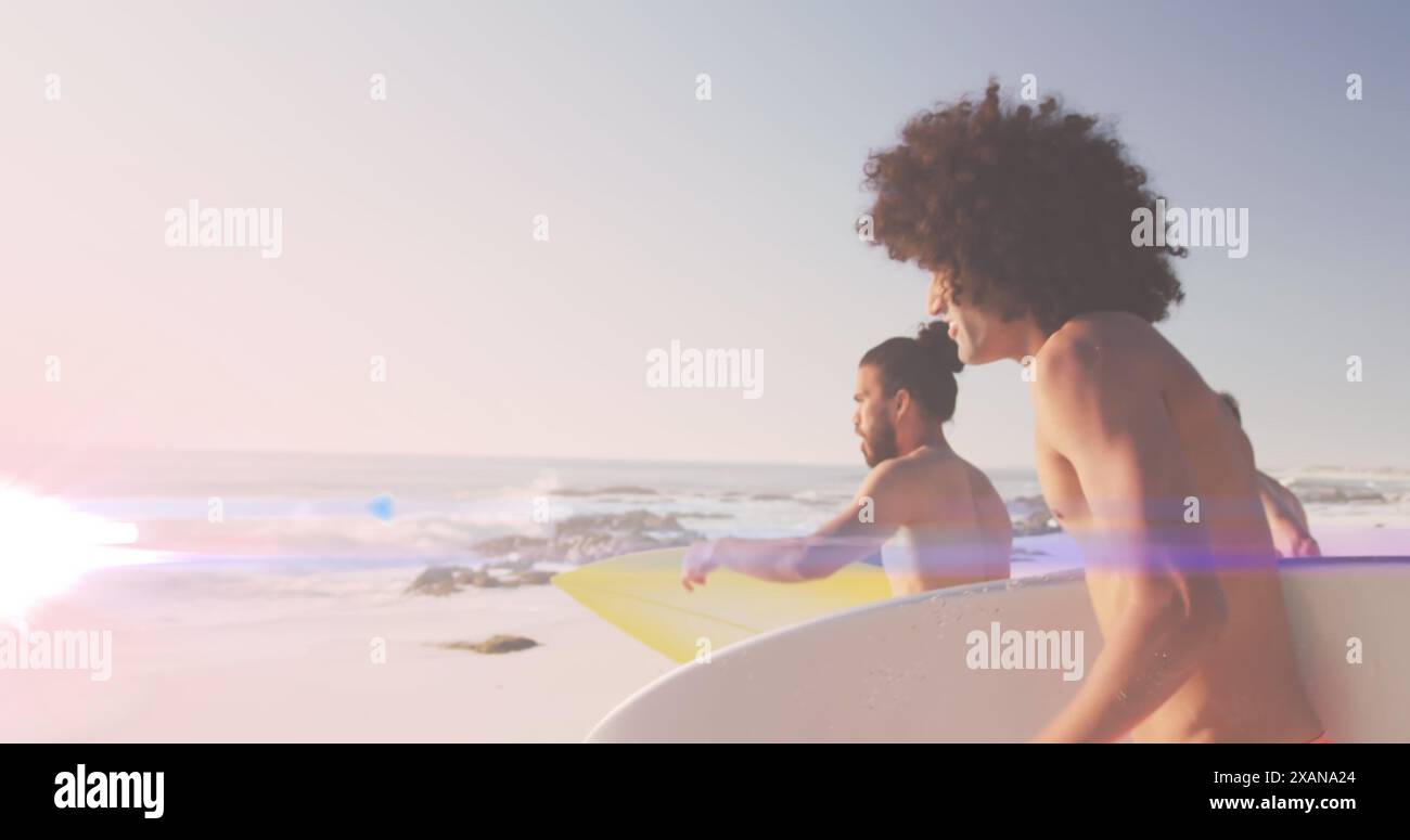 Immagine di luce su amici maschi felici e diversi che corrono sulla spiaggia con tavole da surf Foto Stock