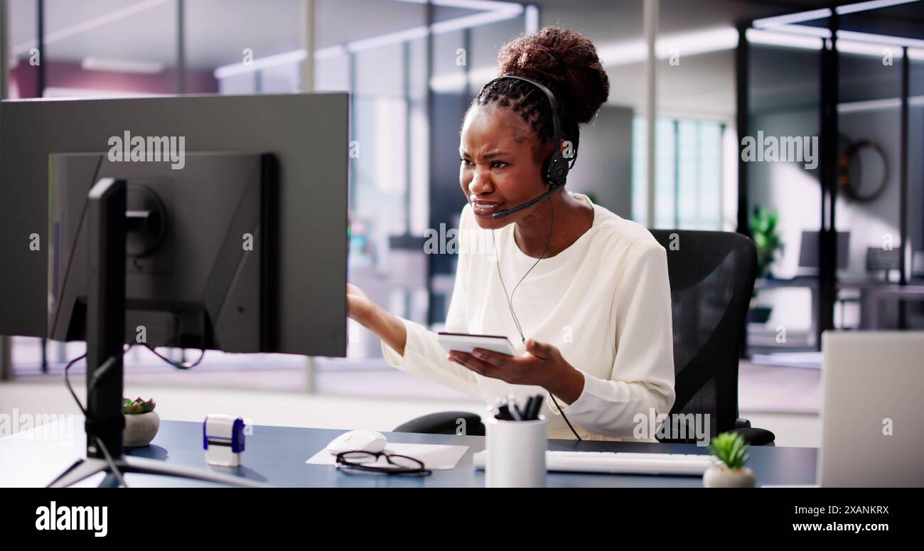 Una donna d'affari afroamericana in ufficio, preoccupata, utilizza le cuffie per videoconferenze, e si è preoccupata di attacchi informatici e protezione dei dati. Foto Stock