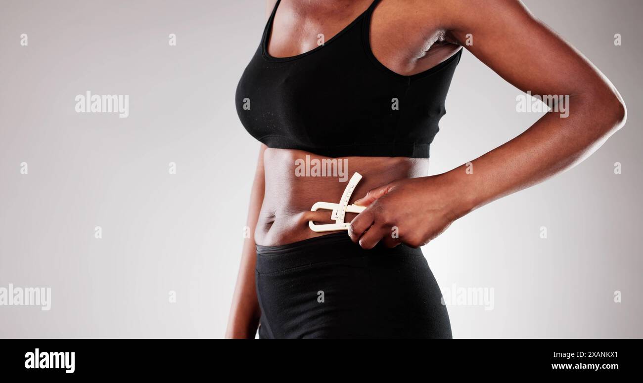 La scultrice del corpo professionale utilizza il calibro per controllare i progressi del viaggio di perdita di peso della donna afroamericana per la pubblicità della clinica bariatrica. Foto Stock