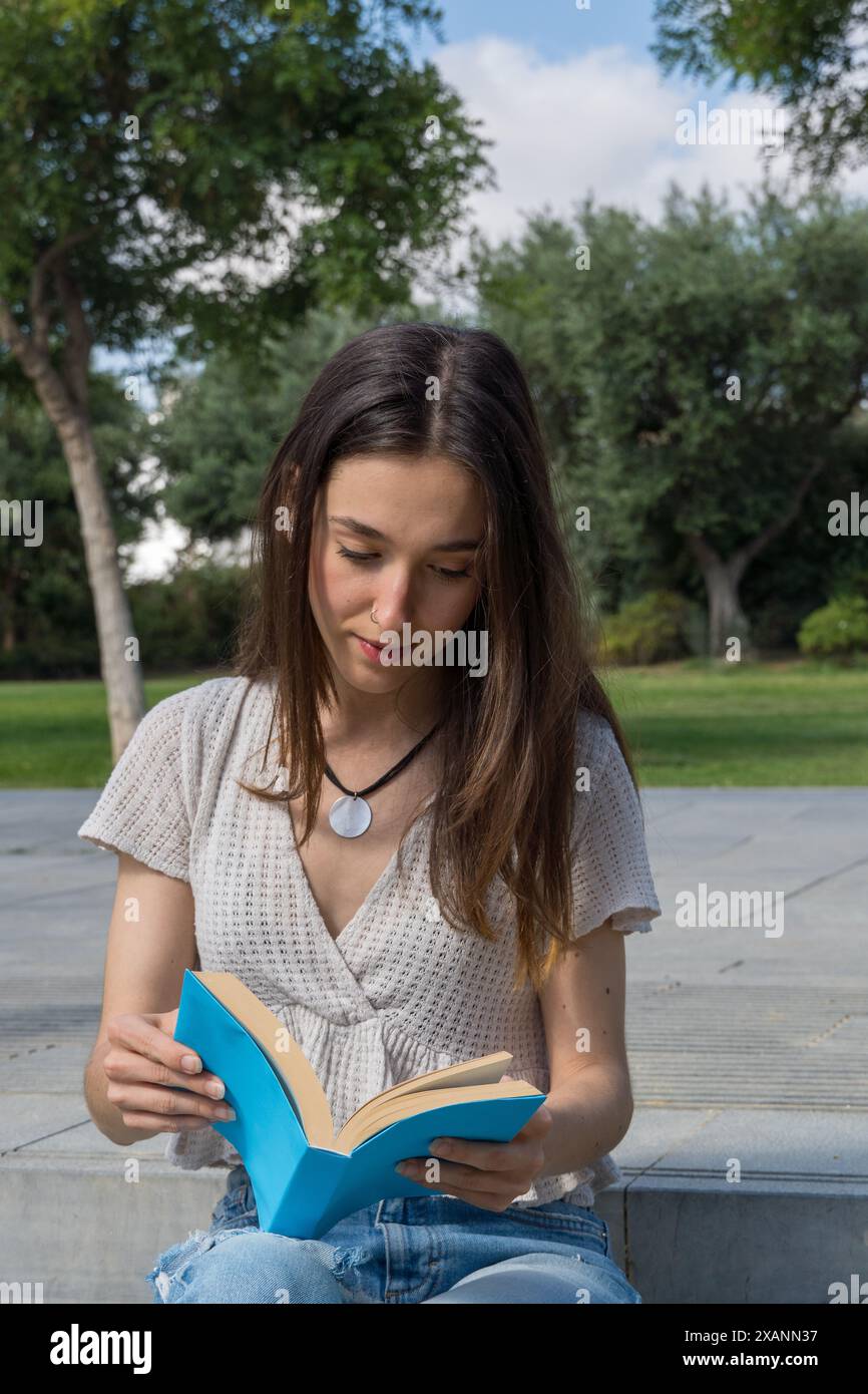 Ragazza del college molto concentrata a leggere un libro nel campus. Vita accademica, istruzione, relax, pausa, studente sull'erba Foto Stock