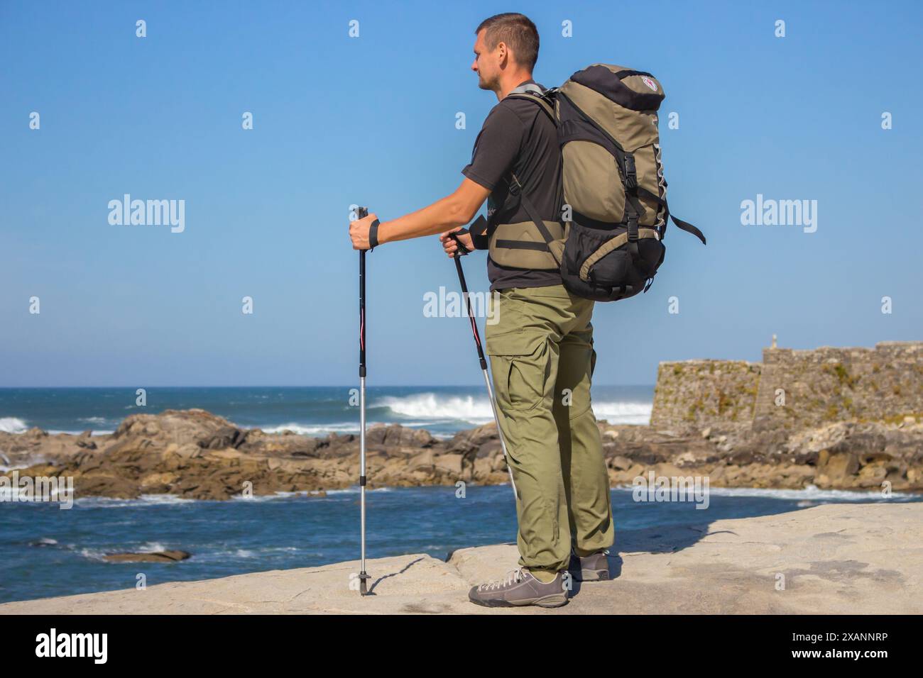 Turista sulla costa atlantica, Portogallo. Pellegrino con zaino e bastoncini sul mare. Viaggia sul Camino de Santiago. Stile di vita attivo. Foto Stock