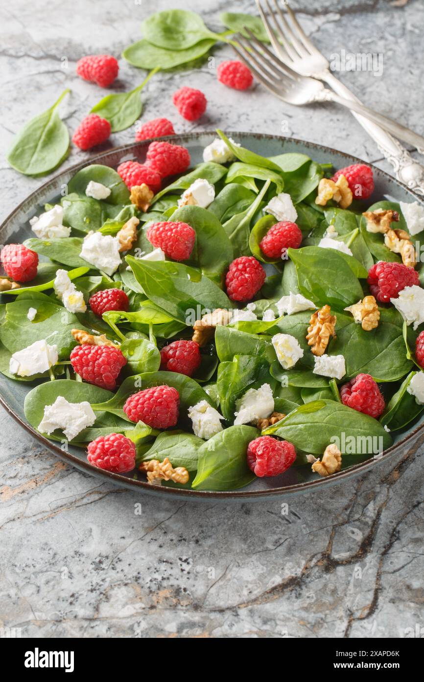 Insalata di spinaci di lamponi con feta e noci da vicino in un piatto sul tavolo. Verticale Foto Stock