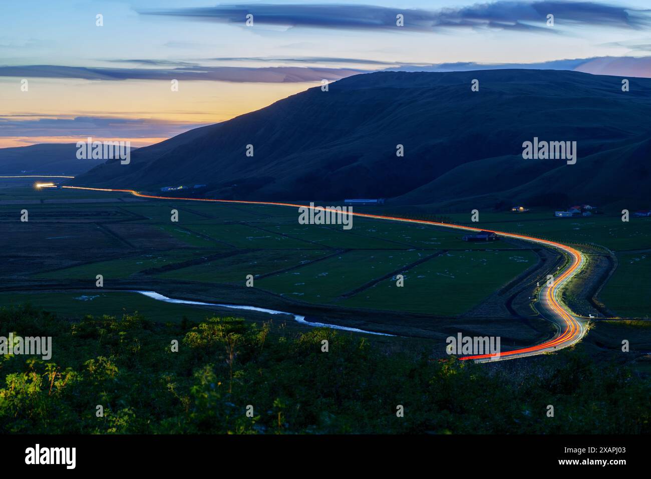 Islanda all'ora blu con Orange Horizon con Long Exposure Car Light Trails on a Road and River Foto Stock