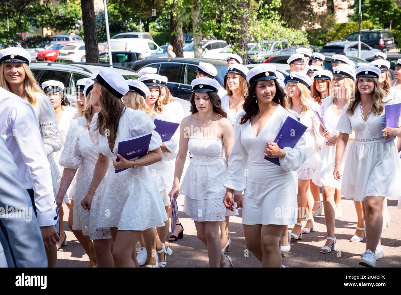 I diplomati della nuova scuola marciano per le strade di Mariehamn dalla loro cerimonia all'edificio principale della scuola per il Åland Graduation Day 2024 al Åland Lyceum (Ålands Gymnasium) a Mariehamn, nell'arcipelago di Åland, nel Mar Baltico, in Finlandia – questo è il giorno in cui gli studenti lasciano la scuola per l'ultima volta. Come parte di questa tradizione nordica, i cartelli sono sormontati con foto dei bambini dei laureati e gli studenti stessi indossano i loro cappelli di laurea in stile marinaio (studentmössa) e vestiti in abiti (ragazzi) e abiti bianchi (ragazze). Foto: Rob Watkins. Foto Stock