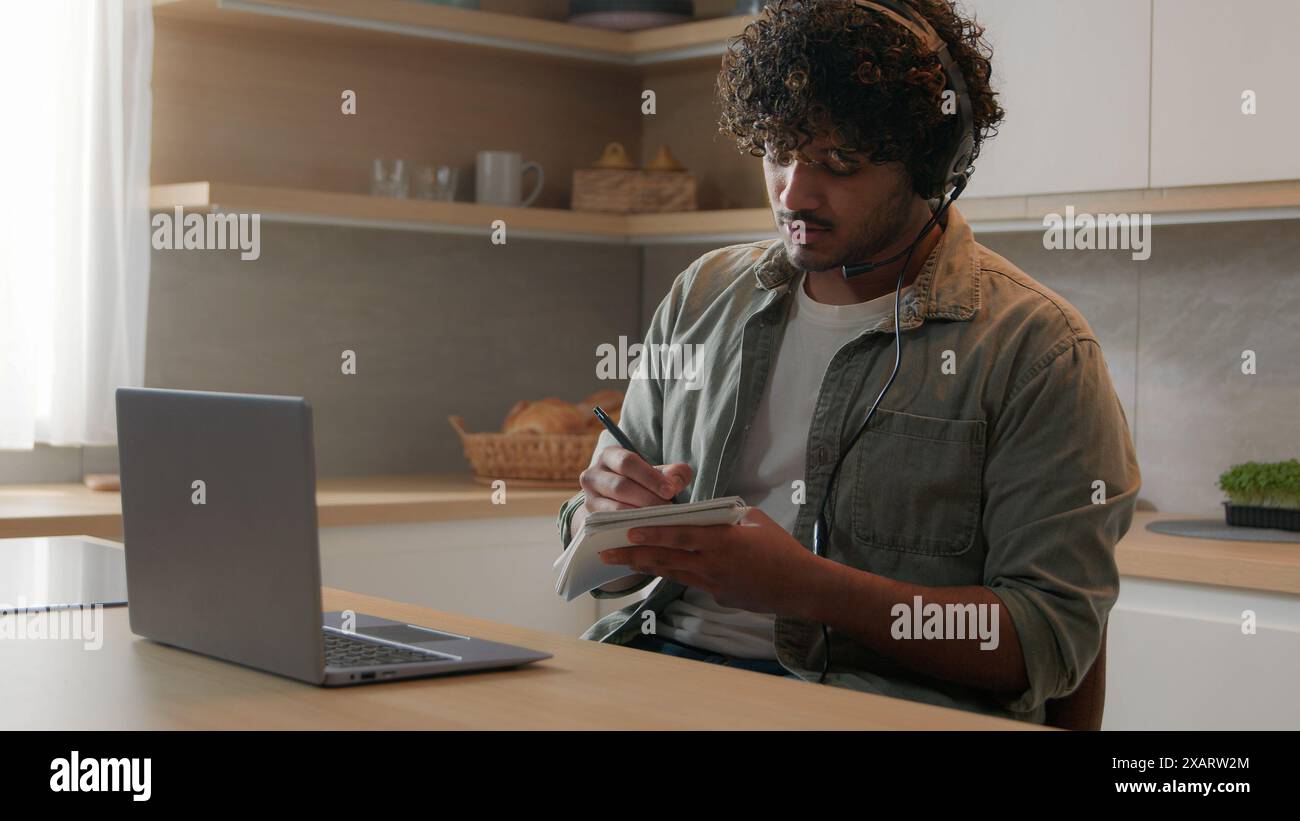 Uomo ispanico con cuffie conferenza portatile sessione di coaching in classe a distanza lezione e-learning studiare online in cucina indiano ragazzo arabo maschio Foto Stock