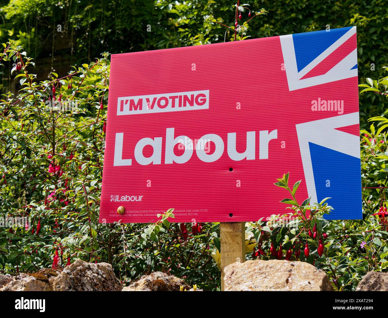 Il cartello "sto votando laburista", dietro un muro di pietra, che promuove il voto per il partito laburista a Faringdon, Oxfordshire, Inghilterra, Regno Unito Foto Stock