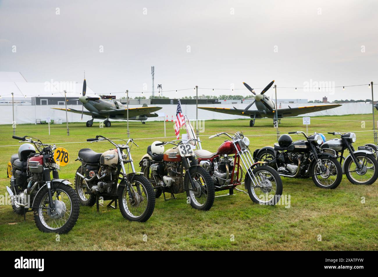 Motociclette Triumph classiche incl. Motociclo americano con la bandiera Stars and Stripes in mostra davanti agli aerei da caccia al Goodwood Revival UK Foto Stock
