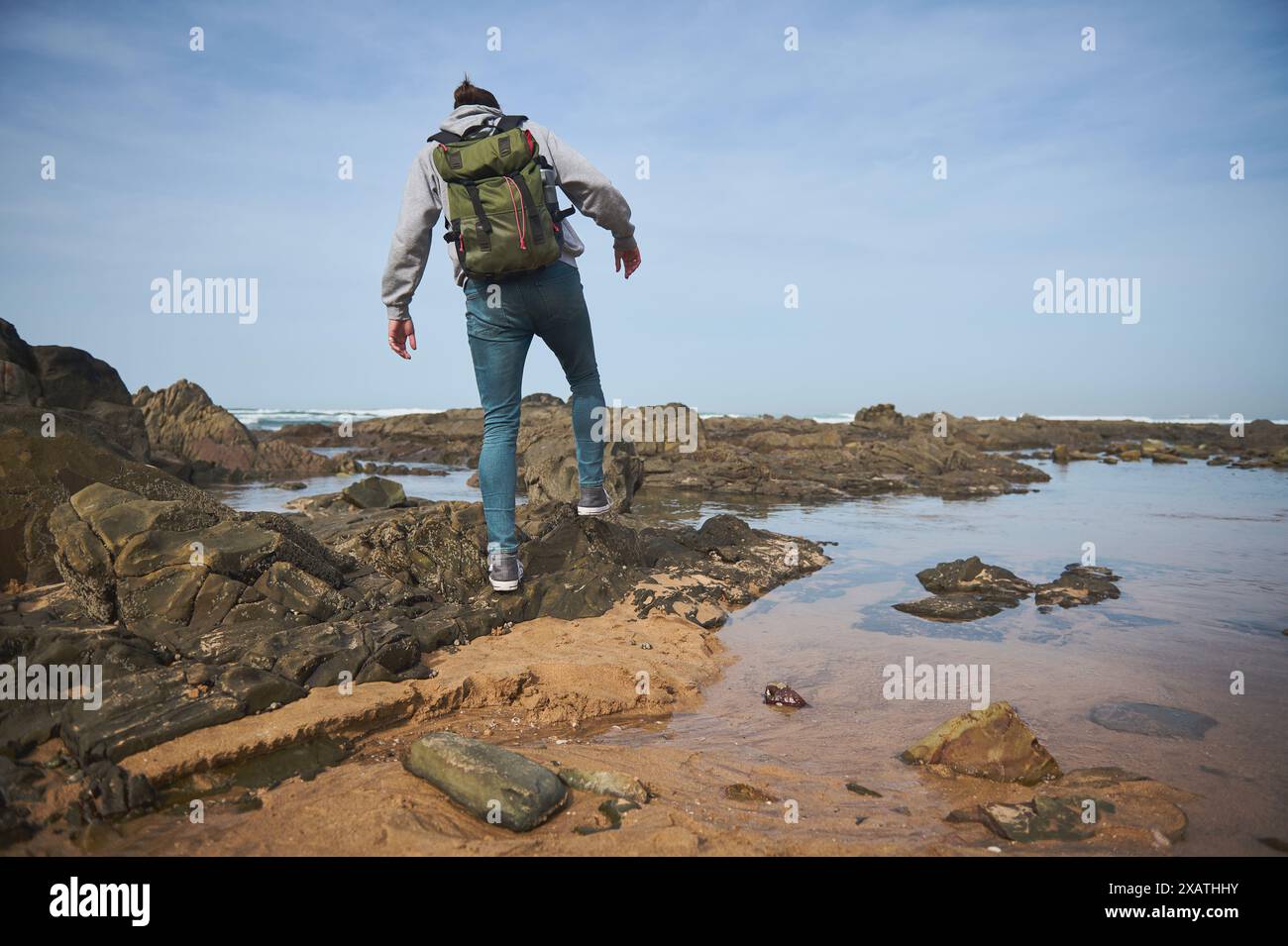 Un giovane con uno zaino che fa trekking attraverso una costa rocciosa sotto un cielo azzurro. Avventura all'aria aperta ed esplorazione nella natura, experi Foto Stock