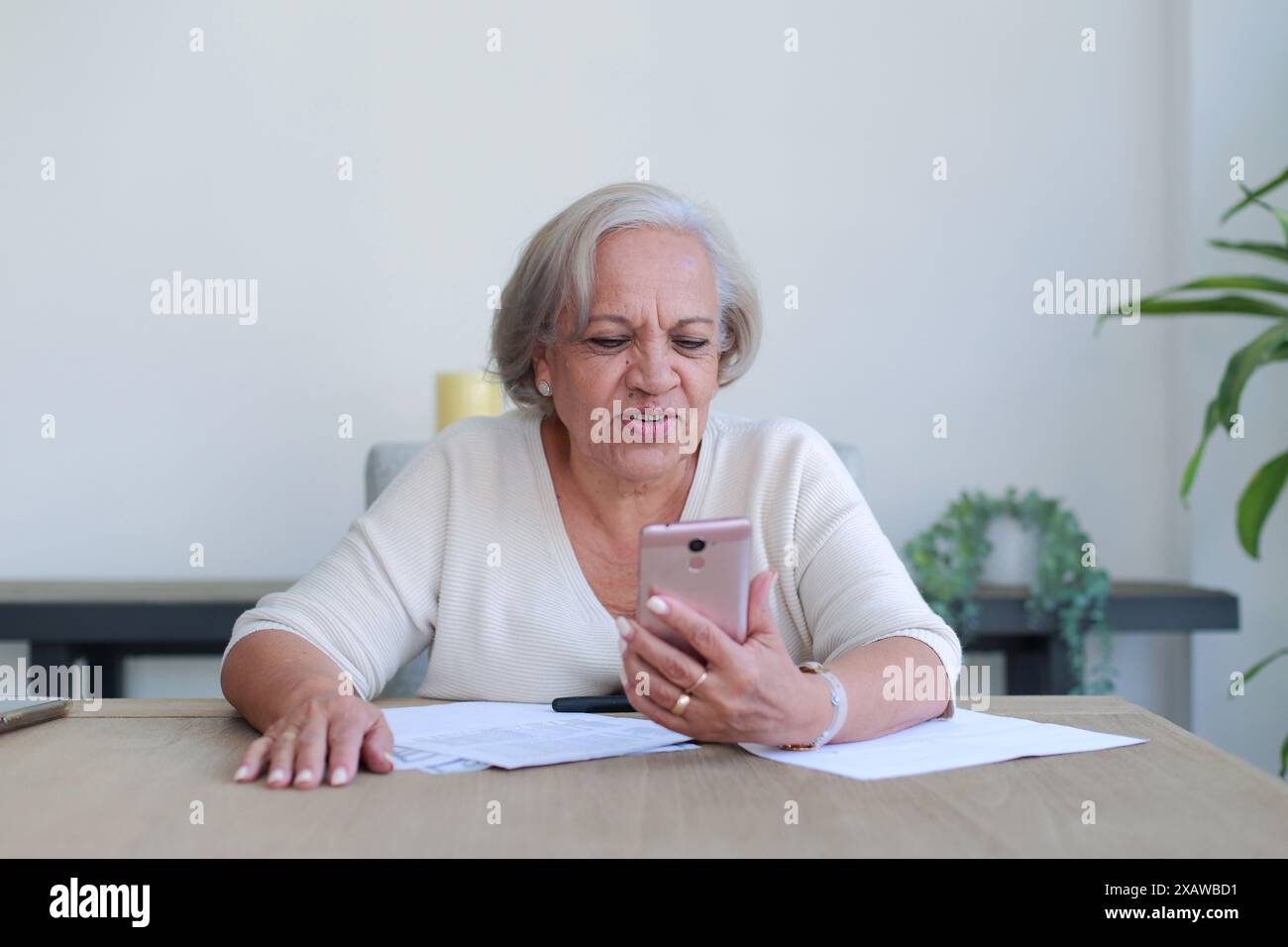 La signora premurosa esamina documenti importanti a casa mentre si utilizza il telefono cellulare Foto Stock