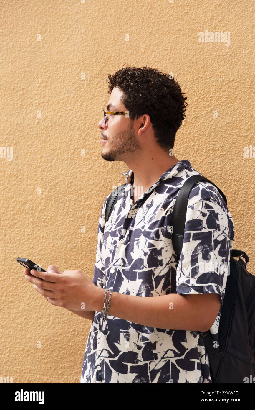 Giovane uomo urbano che cerca con stile utilizzando il suo smartphone in città. Moda urbana, esplorazione urbana, stile di vita moderno Foto Stock