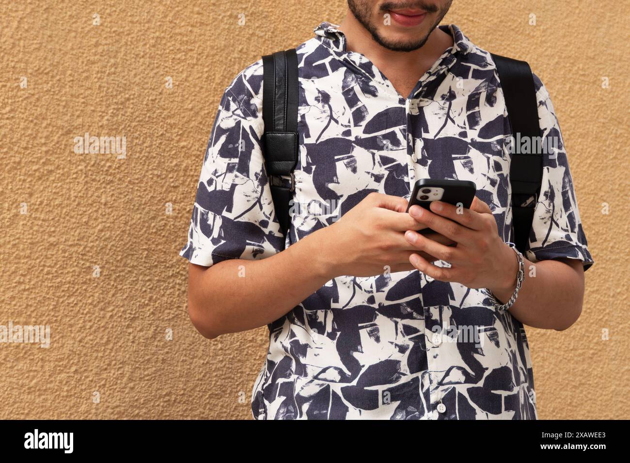 Giovane uomo con una camicia stampata che invia un messaggio con il suo smartphone. Comunicazione mobile, tecnologia, stile moderno Foto Stock