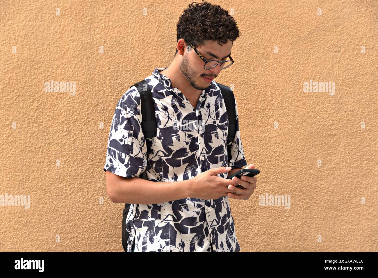 Giovane uomo con camicia e zaino stampati, con smartphone. Stile moderno, moda, tecnologia, gioventù, comunicazione. Foto Stock