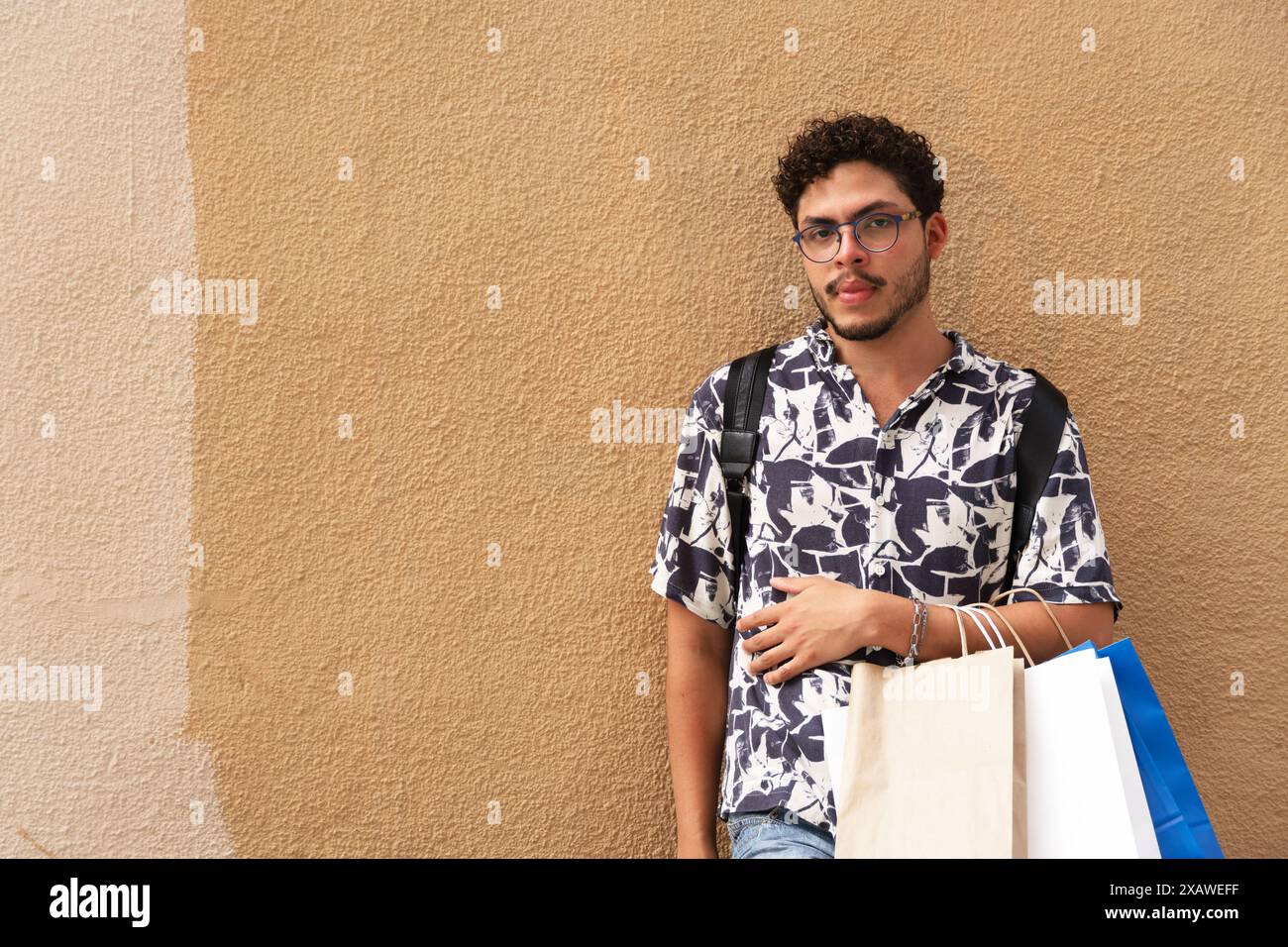 Esplorando la città: Giovane uomo in camicia stampata e borse per lo shopping. Stile urbano, moda, esplorazione Foto Stock
