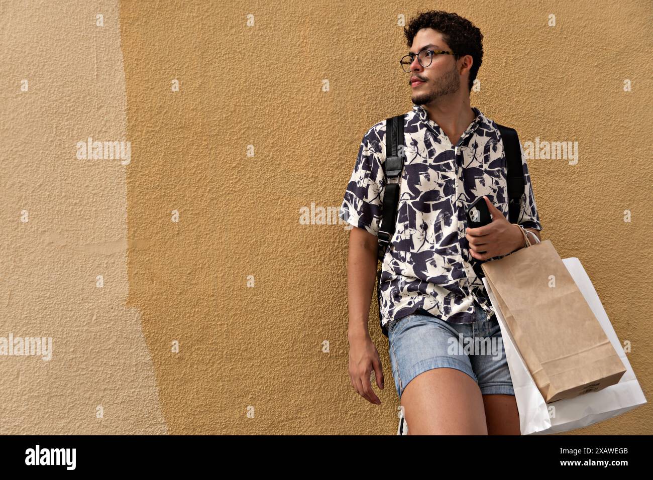 Giovane uomo in stile di vita attivo con camicia stampata e borse per lo shopping. Moda, attività, città Foto Stock