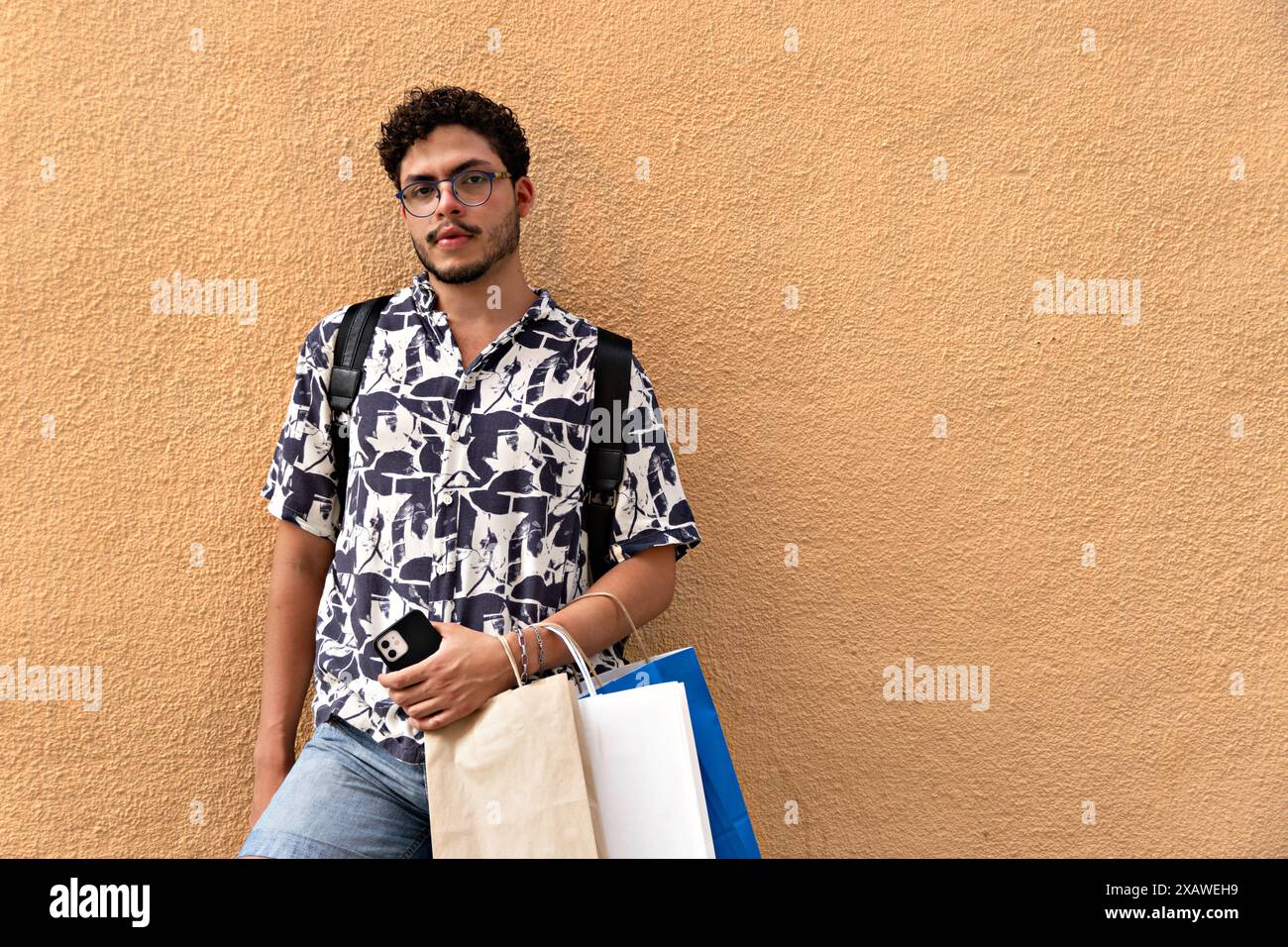 Giovane con zaino e camicia stampata che cerca e riposa. Moda, stile di vita, esplorazione urbana Foto Stock