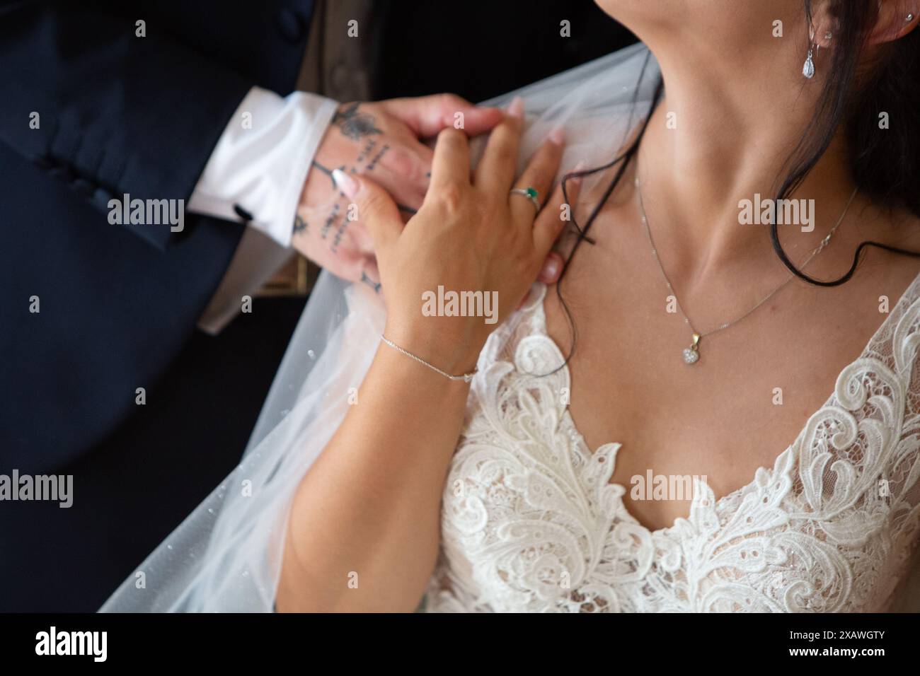 Lo sposo posiziona delicatamente la sua mano tatuata sulla spalla della sposa, mostrando il loro amore e legame nel loro giorno speciale Foto Stock