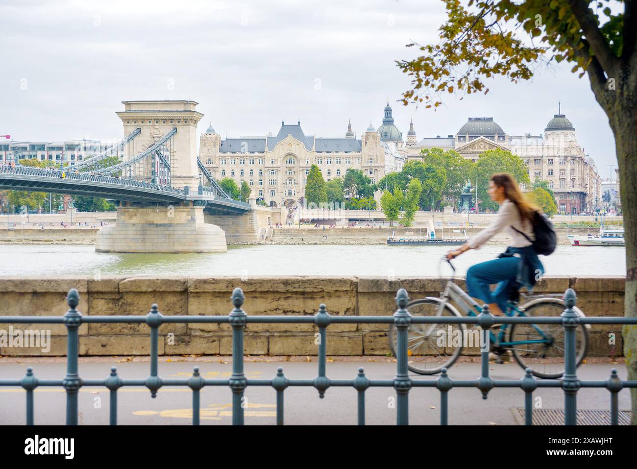 Giovane donna in bicicletta che va contro il Ponte delle catene e il palazzo di Gresham Foto Stock