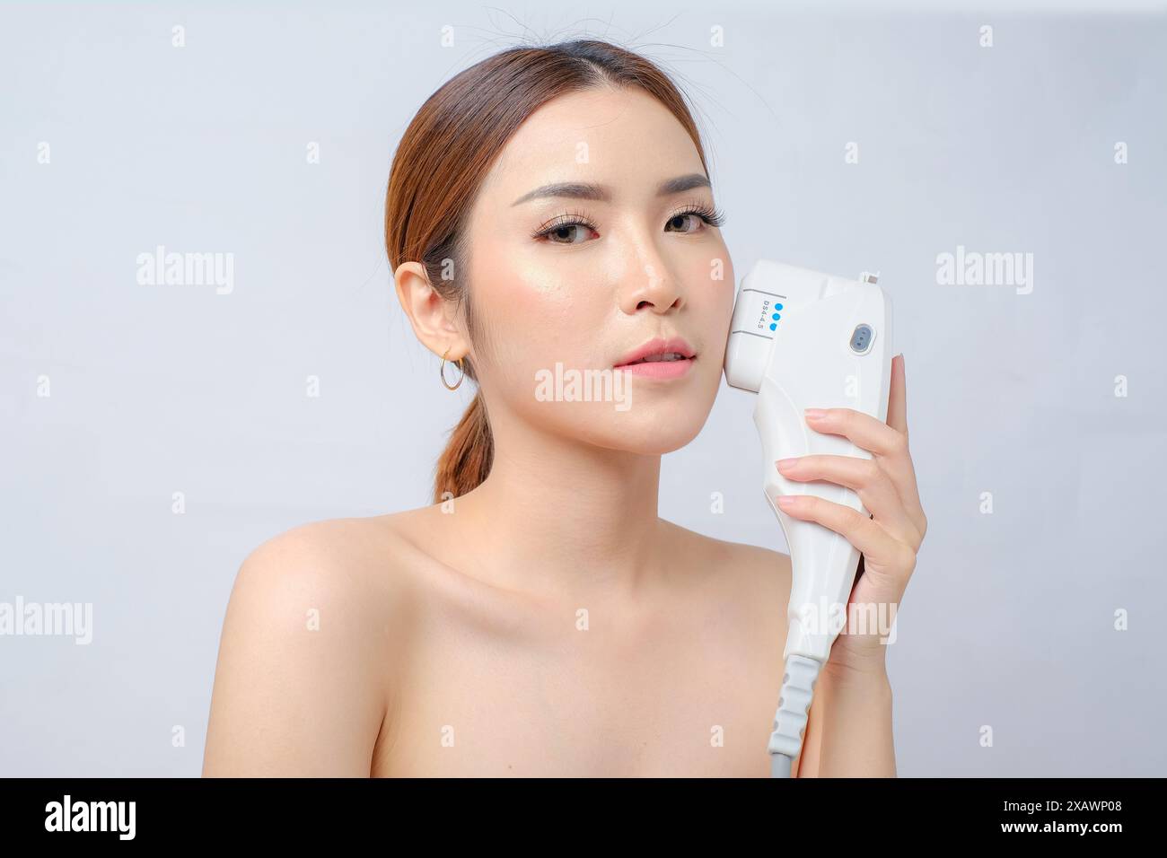 Affascinante donna asiatica che utilizza laser HIFU strumento per il trattamento rassodante della pelle Foto Stock