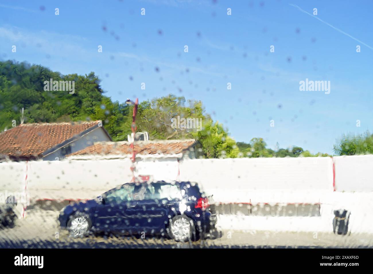 Vetro con gocce d'acqua e strada fuori fuoco sullo sfondo. Una visita ad un autolavaggio manuale - la vista dall'interno dell'auto Foto Stock