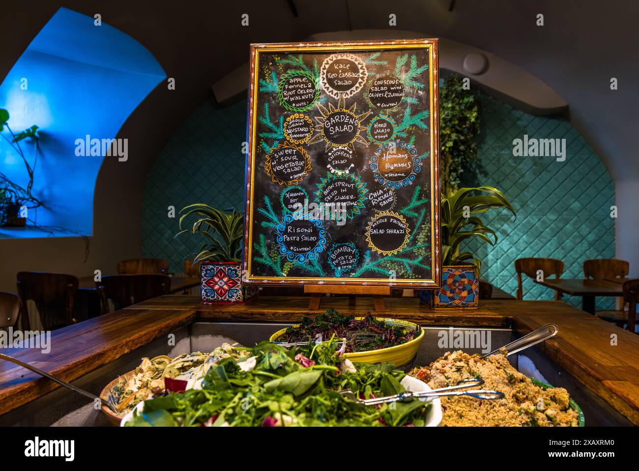 Una lavagna dipinta a mano che elenca i stand del buffet "Insalata del Giardino" nel ristorante Hermans sopra vasi colorati tra le ciotole di insalata. Hermans è un ristorante vegetariano e vegano con un buffet all-you-can-eat per il pranzo, che offre insalate, curry, pane fatto in casa e condimenti vegani tra altri piatti. Il ristorante attribuisce grande importanza agli ingredienti biologici e alla sostenibilità, utilizza prevalentemente materie prime biologiche ed è certificato ambientale. È particolarmente popolare tra i giovani per la sua tariffa piatta di meno di 20 euro. Fjällgatan 23B, Södermalm, Stoccolma, Stockh Foto Stock