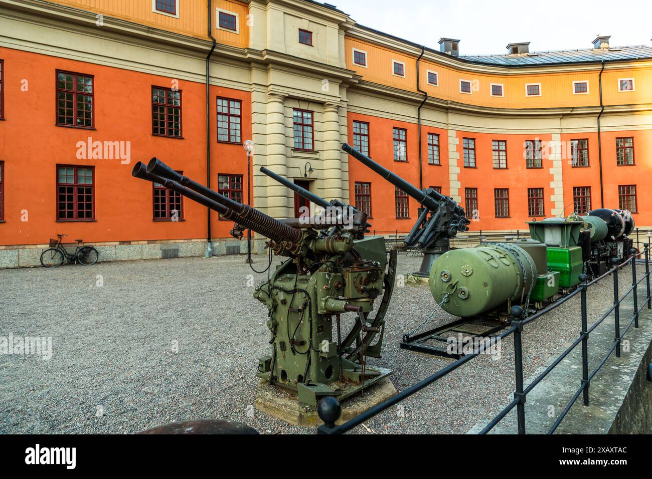 La fortezza di Vaxholm mostra due cannoni antiaerei storici nel suo cortile interno davanti a una facciata di caserma arancione, con una bicicletta appoggiata al muro. Borggården, comune di Vaxholm, Stoccolma, Svezia. Foto Stock