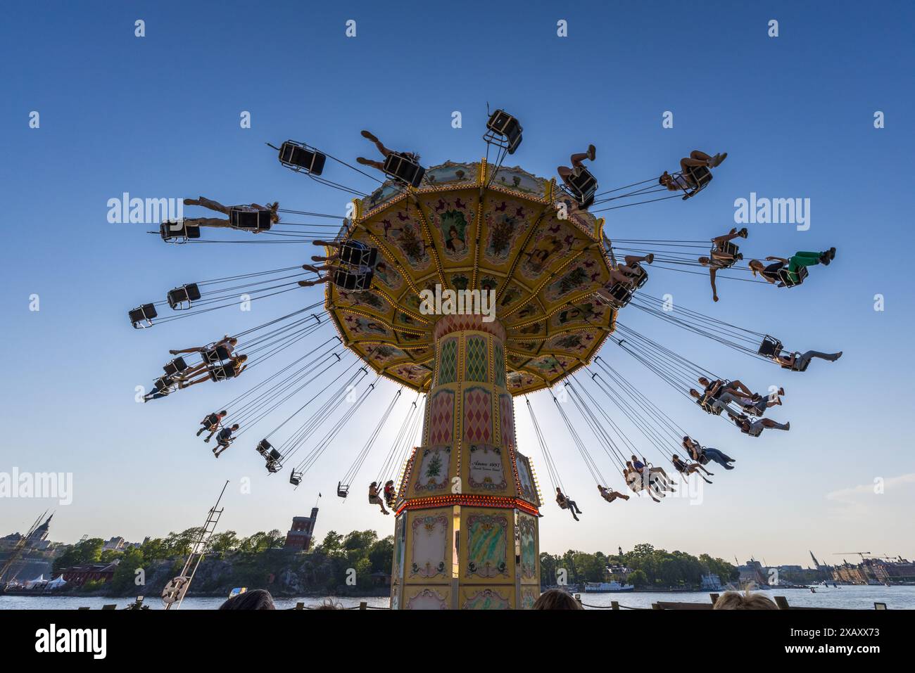 La giostra a catena nostalgica del parco divertimenti Gröna Lund gira al sole della sera, proprio sopra l'acqua. Gröna Lund sull'isola museo di Djurgården è il più antico parco divertimenti della Svezia, fondato nel 1883 da Jacob Schultheiss, nato in Germania, ed è diviso in una sezione vecchia e una nuova. Djurgårdsstaden, Stoccolma, Contea di Stoccolma, Svezia. Foto Stock