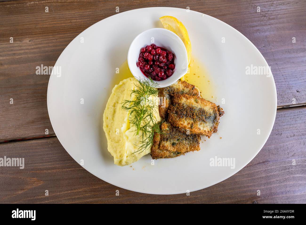 Pesce al forno con purè di patate e mirtilli rossi viene servito come pranzo tradizionale svedese al ristorante giardino Lasse I Parken a Hornstull, Södermalm. Un rametto di aneto decora il pesce impanato accanto a una fetta di limone. Bergsund, Stoccolma, Contea di Stoccolma, Svezia. Foto Stock