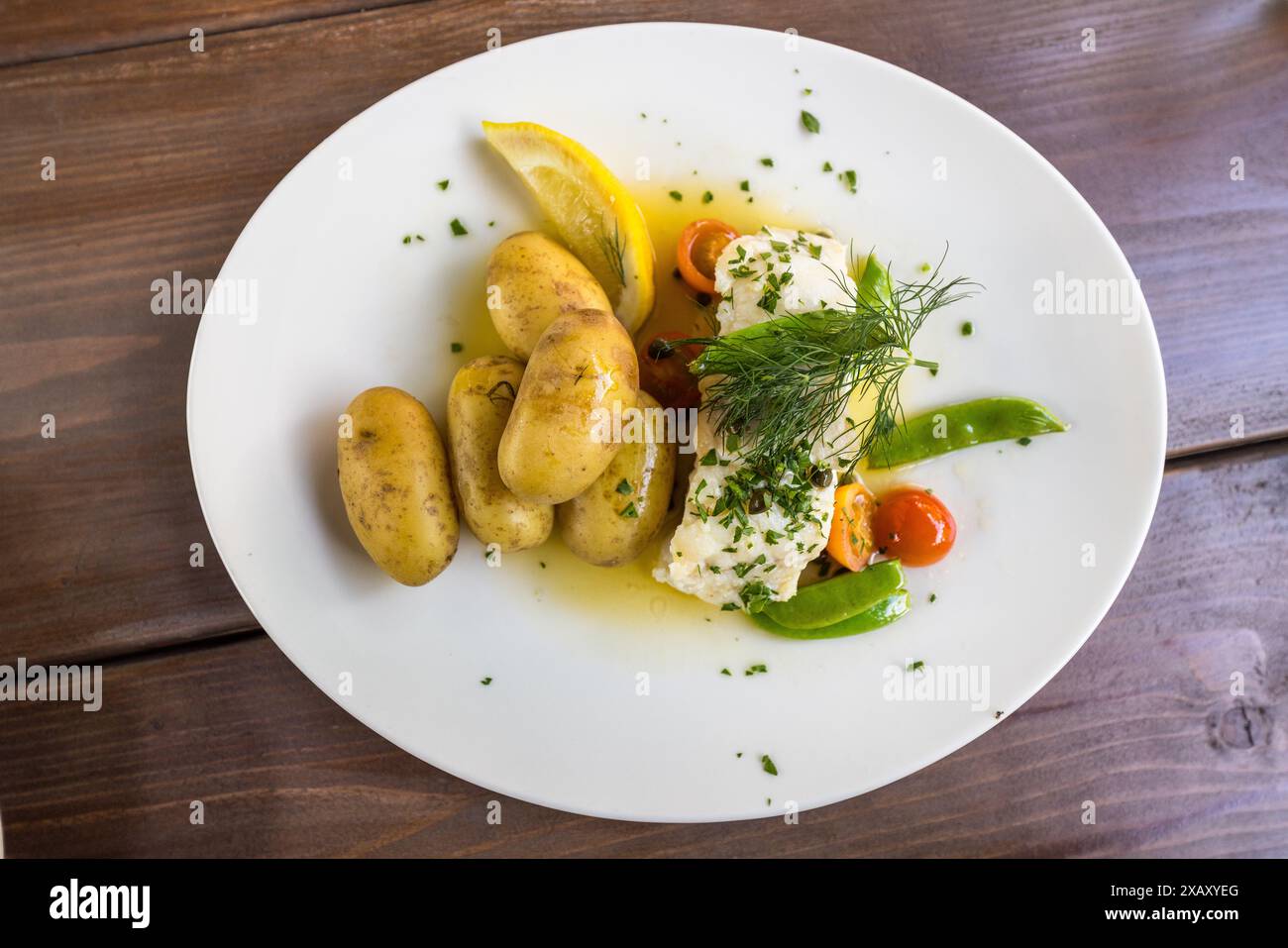 Un piatto di pesce con patate e verdure viene servito nel ristorante del giardino Lasse I Parken a Hornstull, Södermalm. Il piatto contiene piccole patate nuove, un filetto di pesce poch&eacute; con erbe e pomodorini, piselli mangiatutto e una fetta di limone. Bergsund, Stoccolma, Contea di Stoccolma, Svezia. Foto Stock