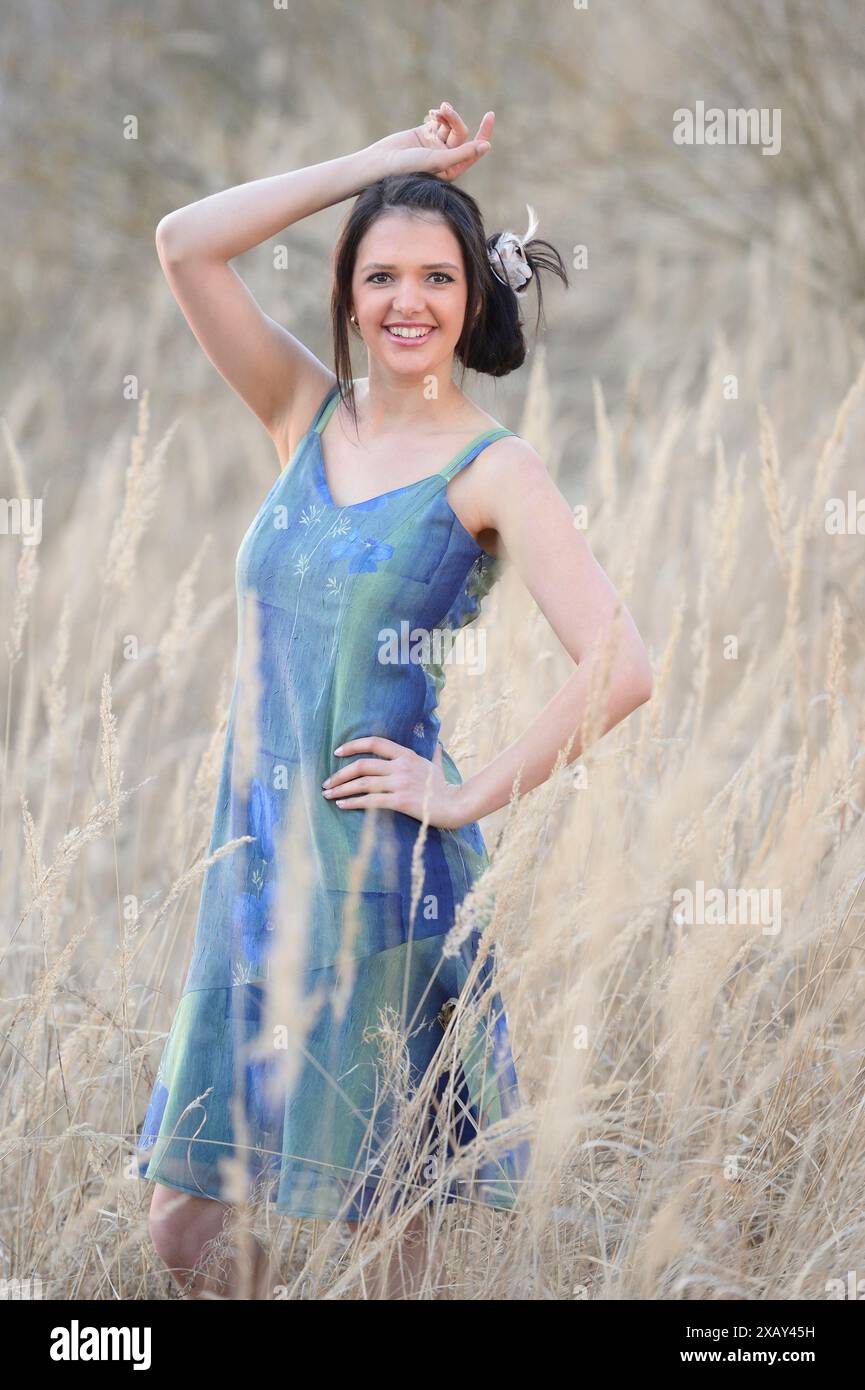 Una giovane donna con un vestito colorato posa in un campo di canne con una mano sul fianco, la Baviera Foto Stock Una giovane donna con un vestito colorato posa in un campo di canne con una mano sul fianco, la Baviera Foto Stock
