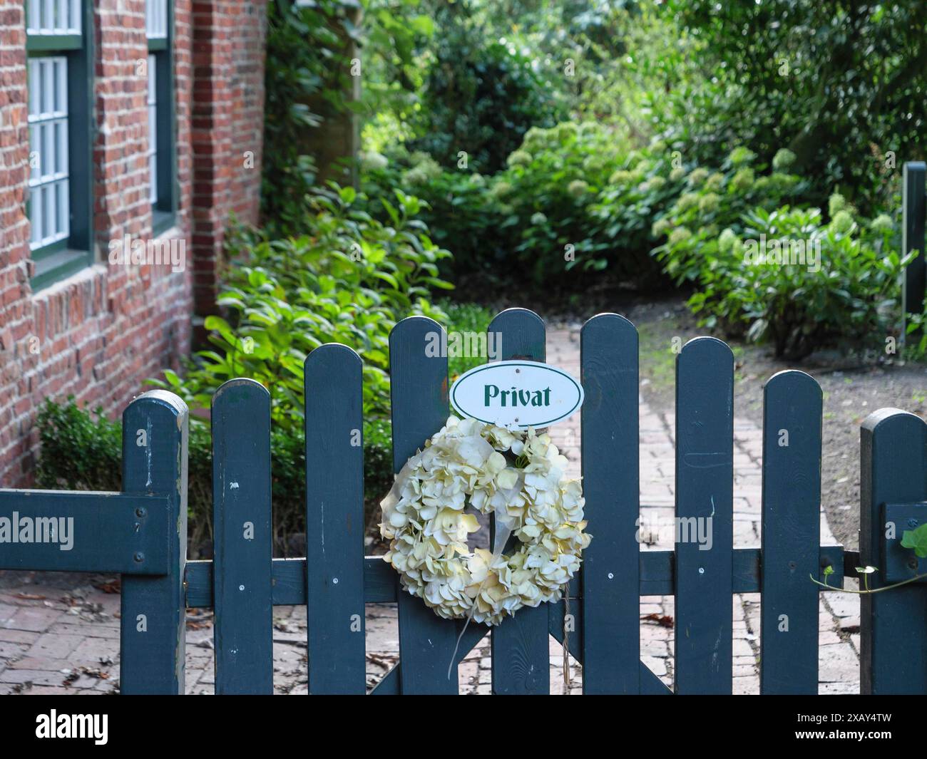 Una recinzione da giardino con un cartello "privato", decorata con una corona di fiori, circondata da piante, Spiekeroog, Frisia orientale, GERMANIA Foto Stock