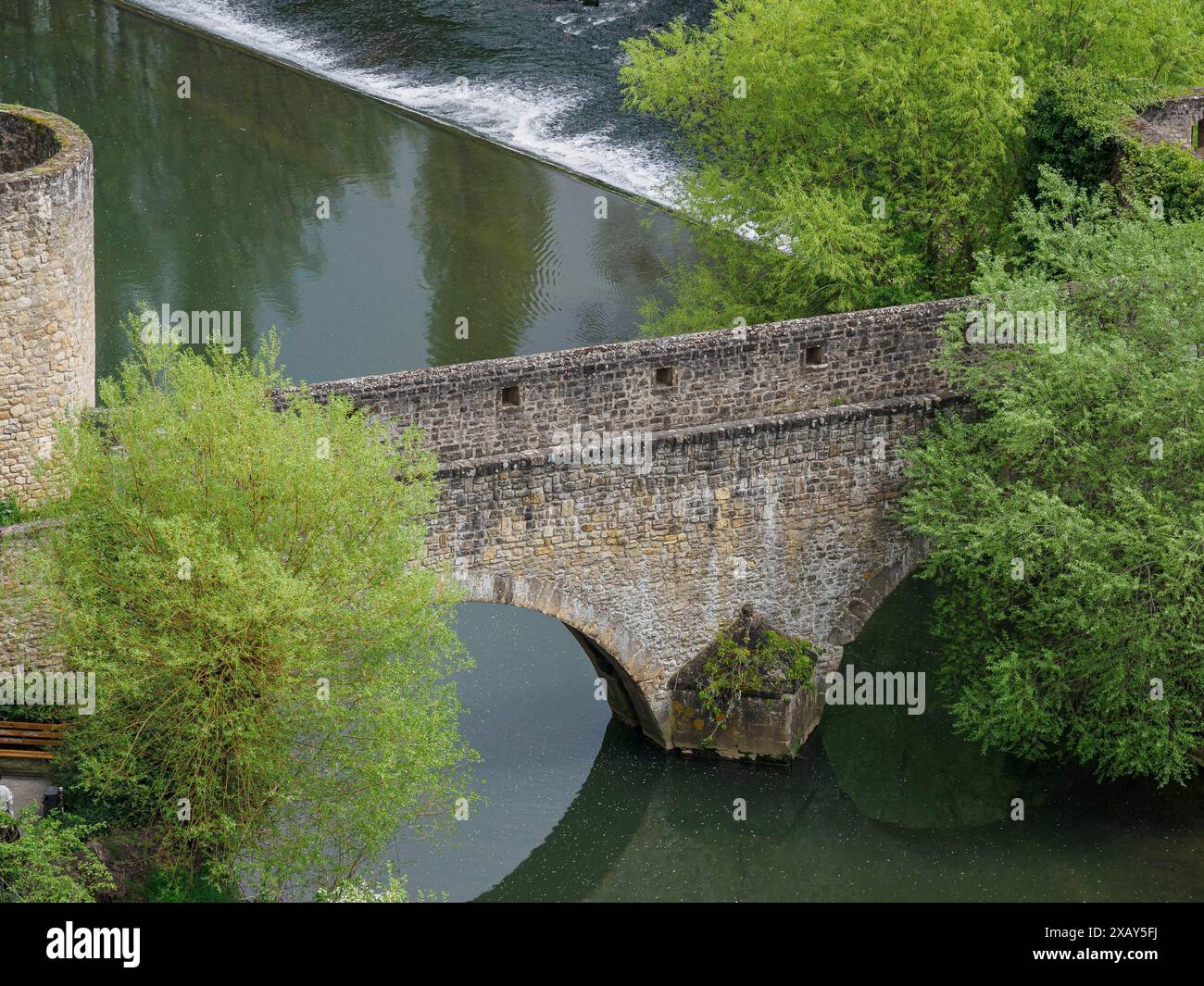 Un vecchio ponte di pietra che attraversa un fiume, circondato da alberi lussureggianti, Lussemburgo, Lussemburgo Foto Stock