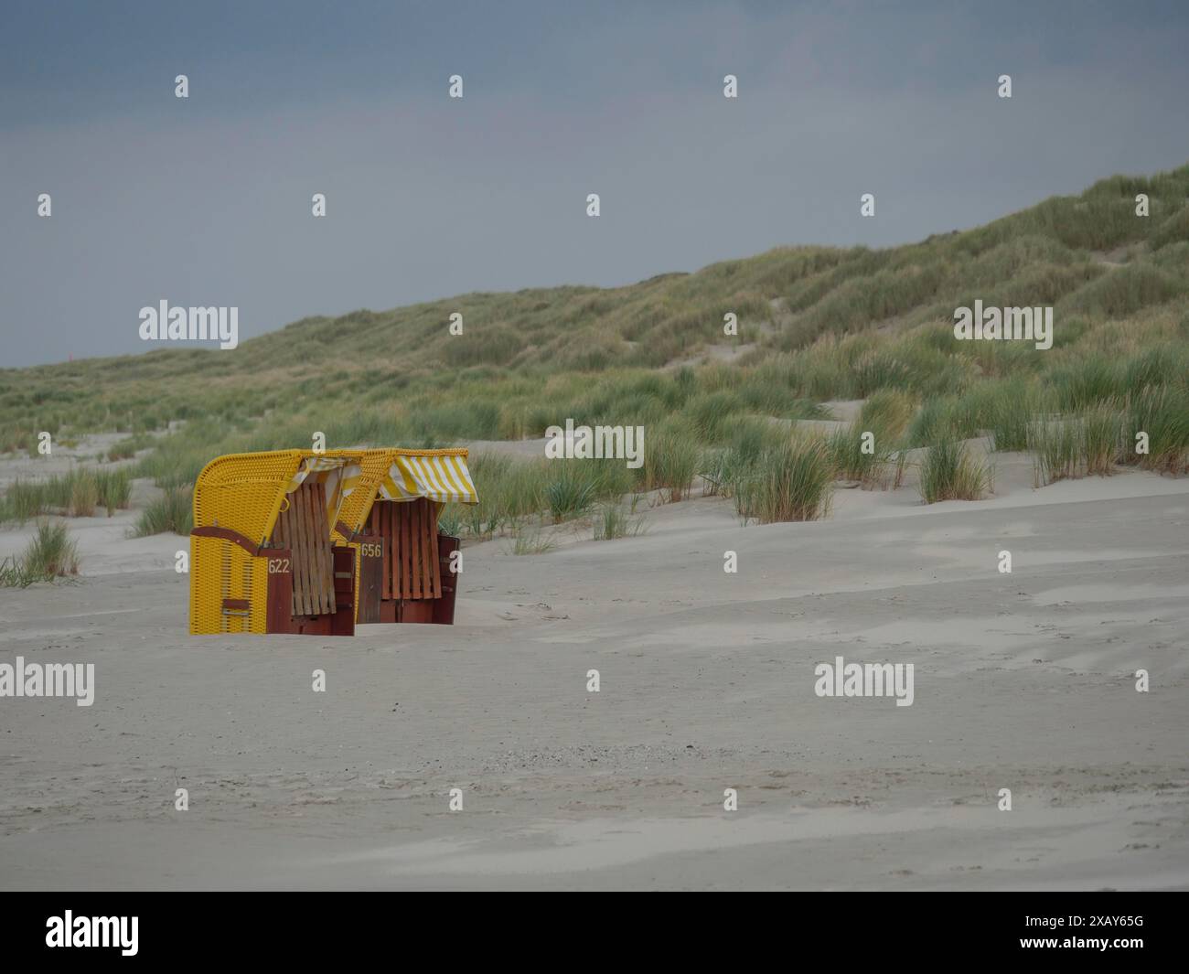 Foto in spiaggia con due sdraio gialle su un'ampia area sabbiosa di fronte alle dune e sotto un cielo nuvoloso, juist, frisia orientale, germania Foto Stock