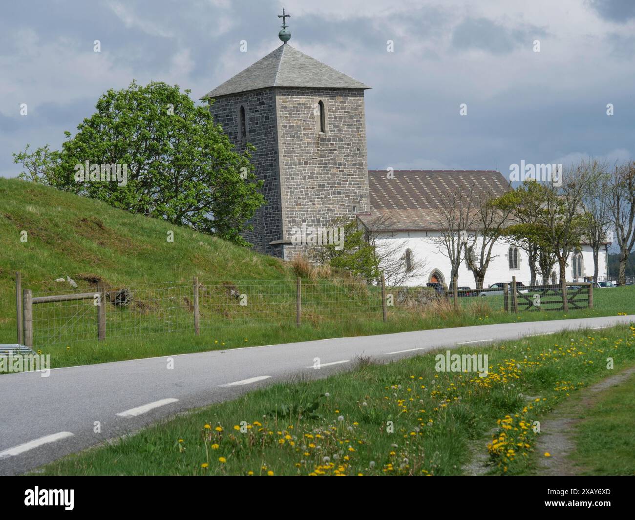 Chiesa in pietra accanto a una strada di campagna, circondata da prati e alberi in primavera, Haugesund, norvegia Foto Stock