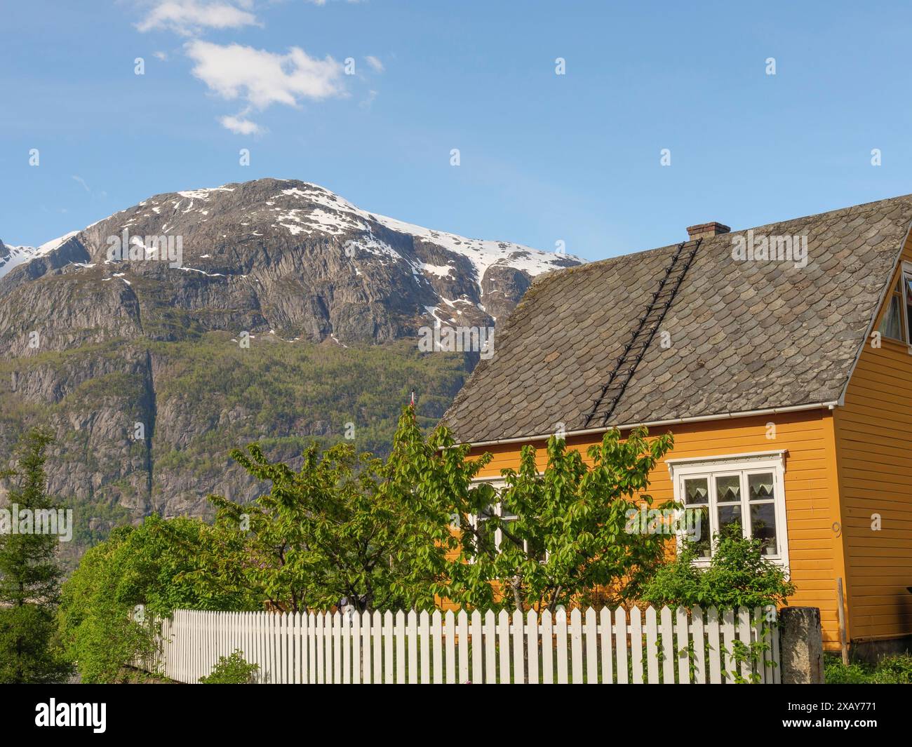 Una casa gialla con una recinzione bianca di fronte a un paesaggio montano sotto un cielo blu, Eidfjord NOR 3 Foto Stock