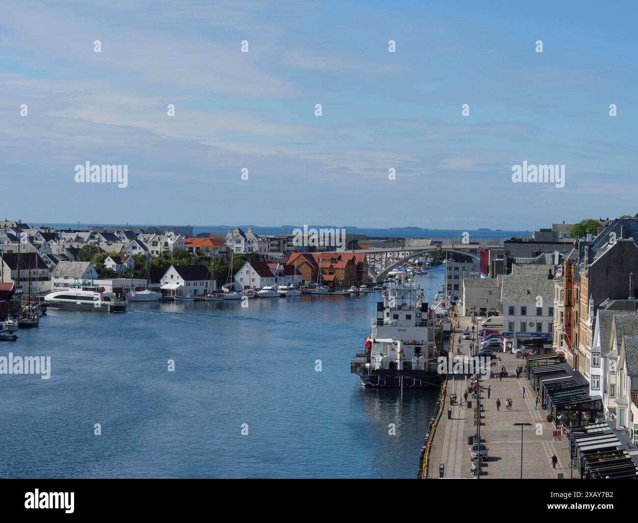 Vista di una città portuale con una passeggiata che mostra edifici e barche lungo la costa, sotto un cielo blu, Haugesund, Norvegia Foto Stock