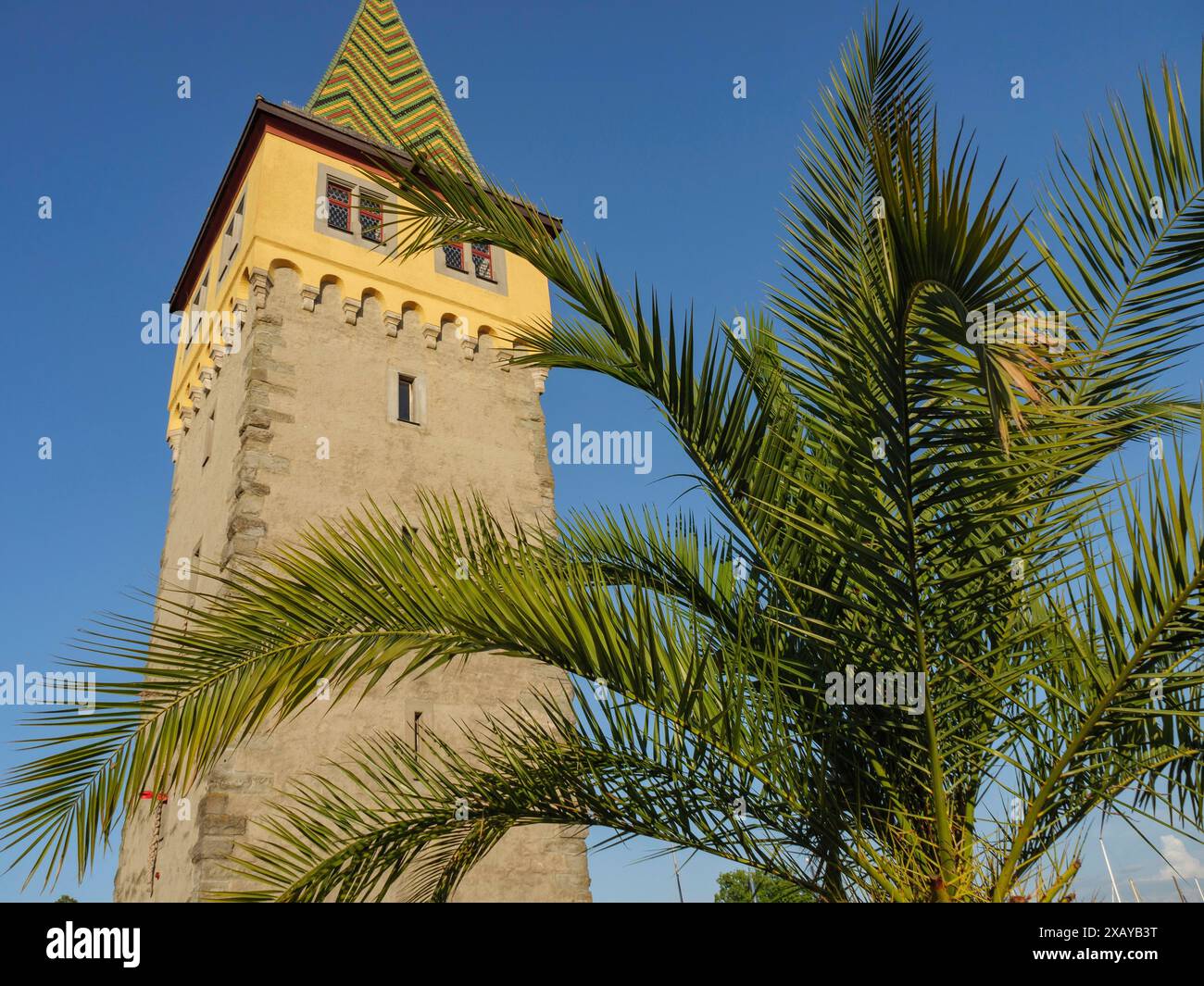 Torre storica con tetto giallo e palme in primo piano sotto un cielo limpido, Meersburg, Lago di Costanza, Germania Foto Stock