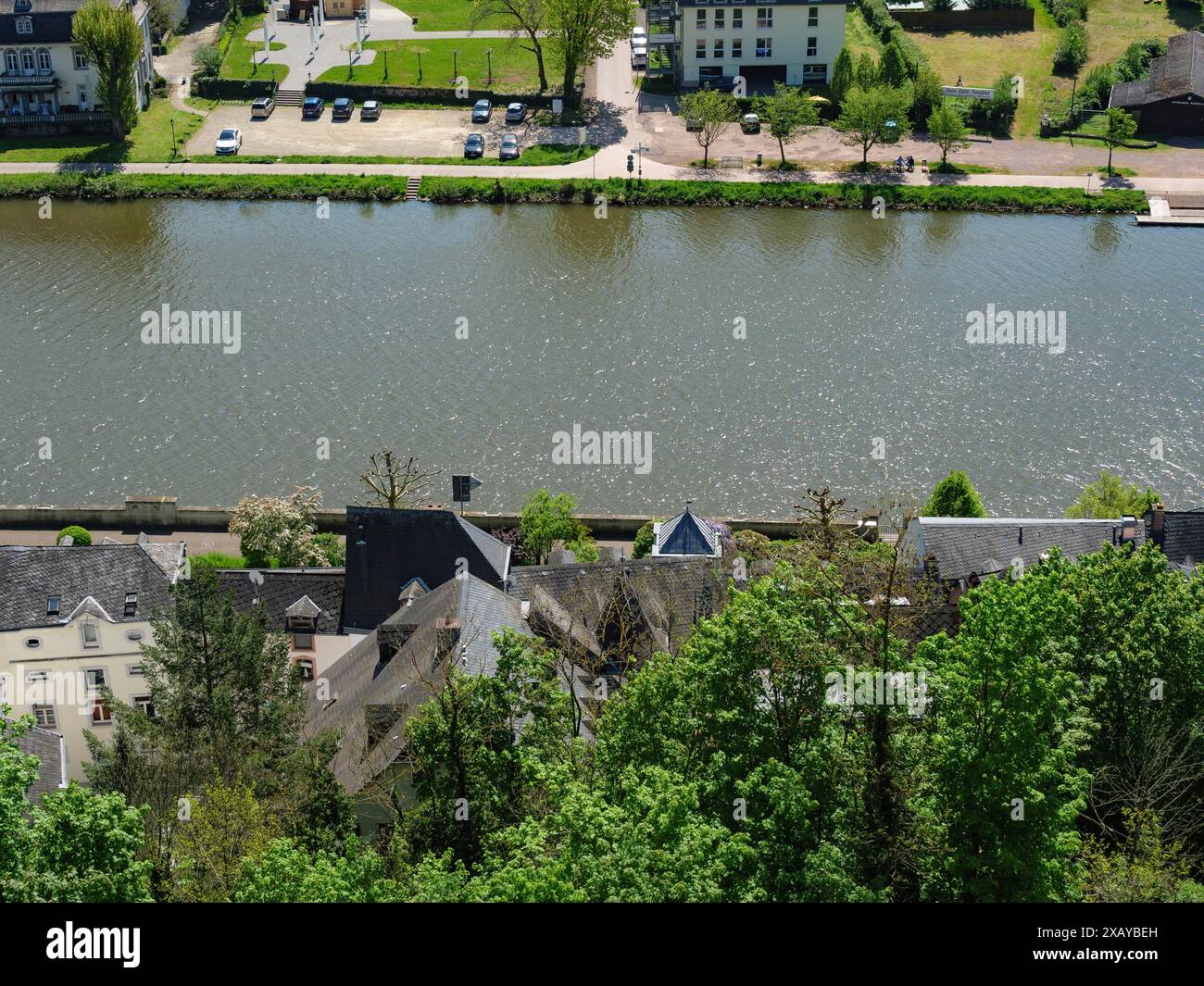 Una vista delle case lungo un fiume, fiancheggiate da alberi e piante verdi, segno di crescita primaverile, Saarburg, germania Foto Stock
