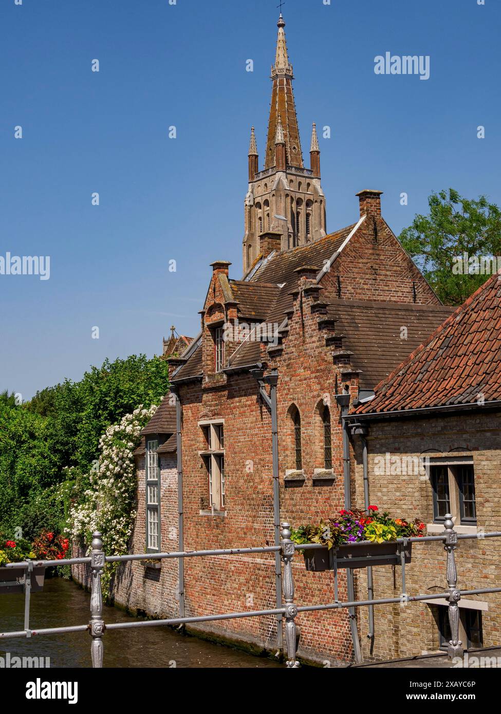 Pittoresca scena con un canale, fiori e un ponte sullo sfondo di una torre della chiesa, Bruges, Belgio Foto Stock