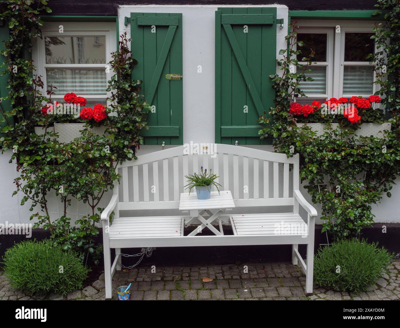 Panca bianca di fronte a una casa con persiane verdi e fiori rossi crea un invitante fascino rurale, Herten, Renania settentrionale-Vestfalia, Germania Foto Stock