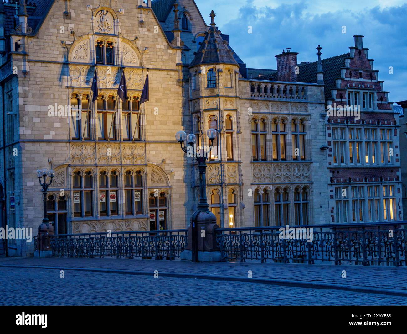 Edifici storici con intricati dettagli gotici e finestre illuminate al crepuscolo, Gand, Belgio Foto Stock