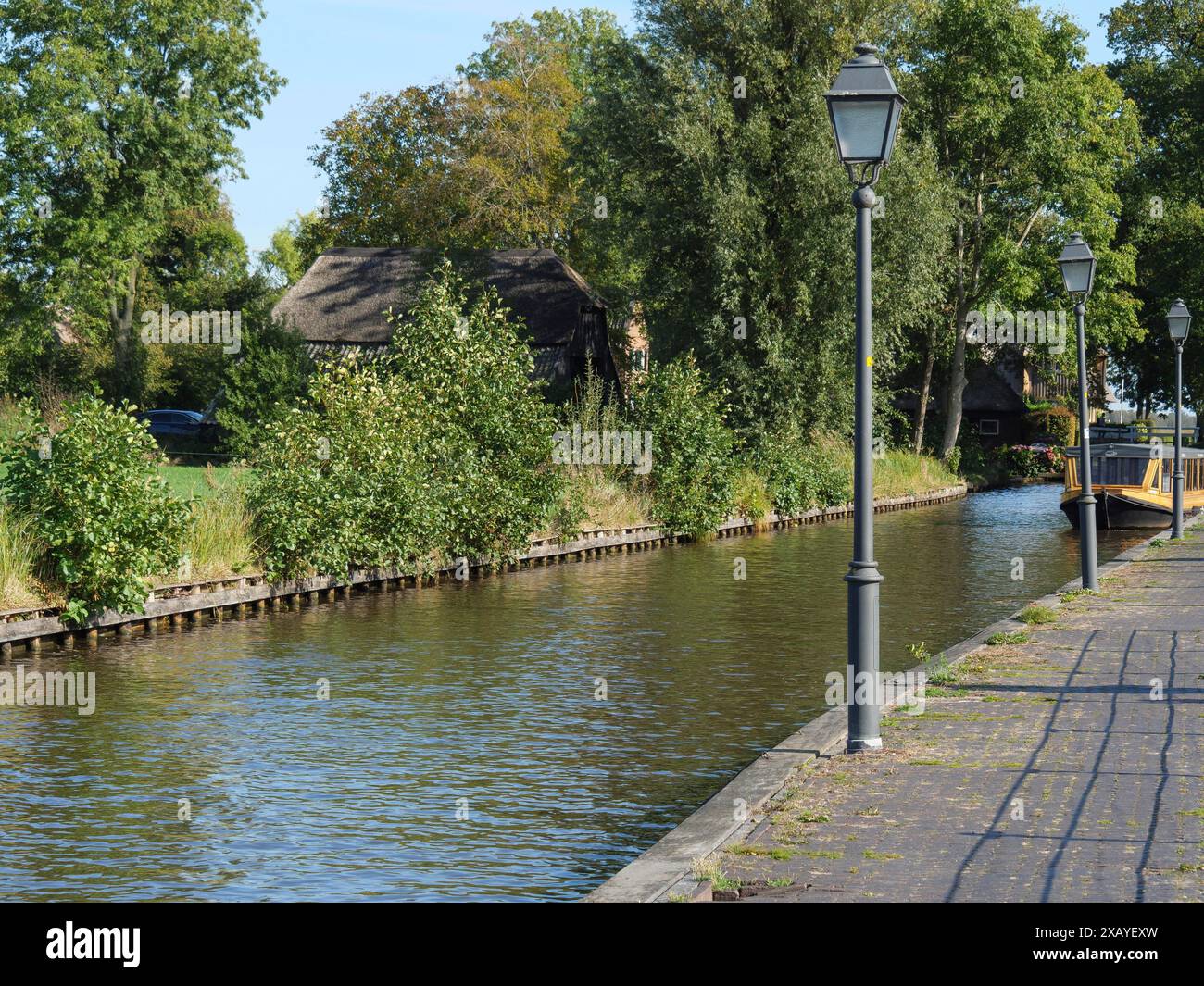 Una passerella pavimentata con lanterne conduce lungo un canale, fiancheggiato da alberi e case, Giethoorn, Paesi Bassi Foto Stock