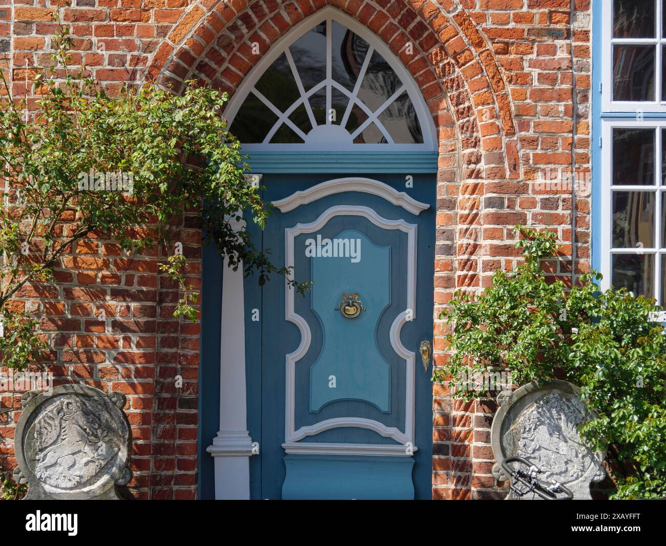 Porta con arco decorativo ed elementi dipinti di blu, circondata da pareti e piante in mattoni rossi, lueneburg, germania Foto Stock
