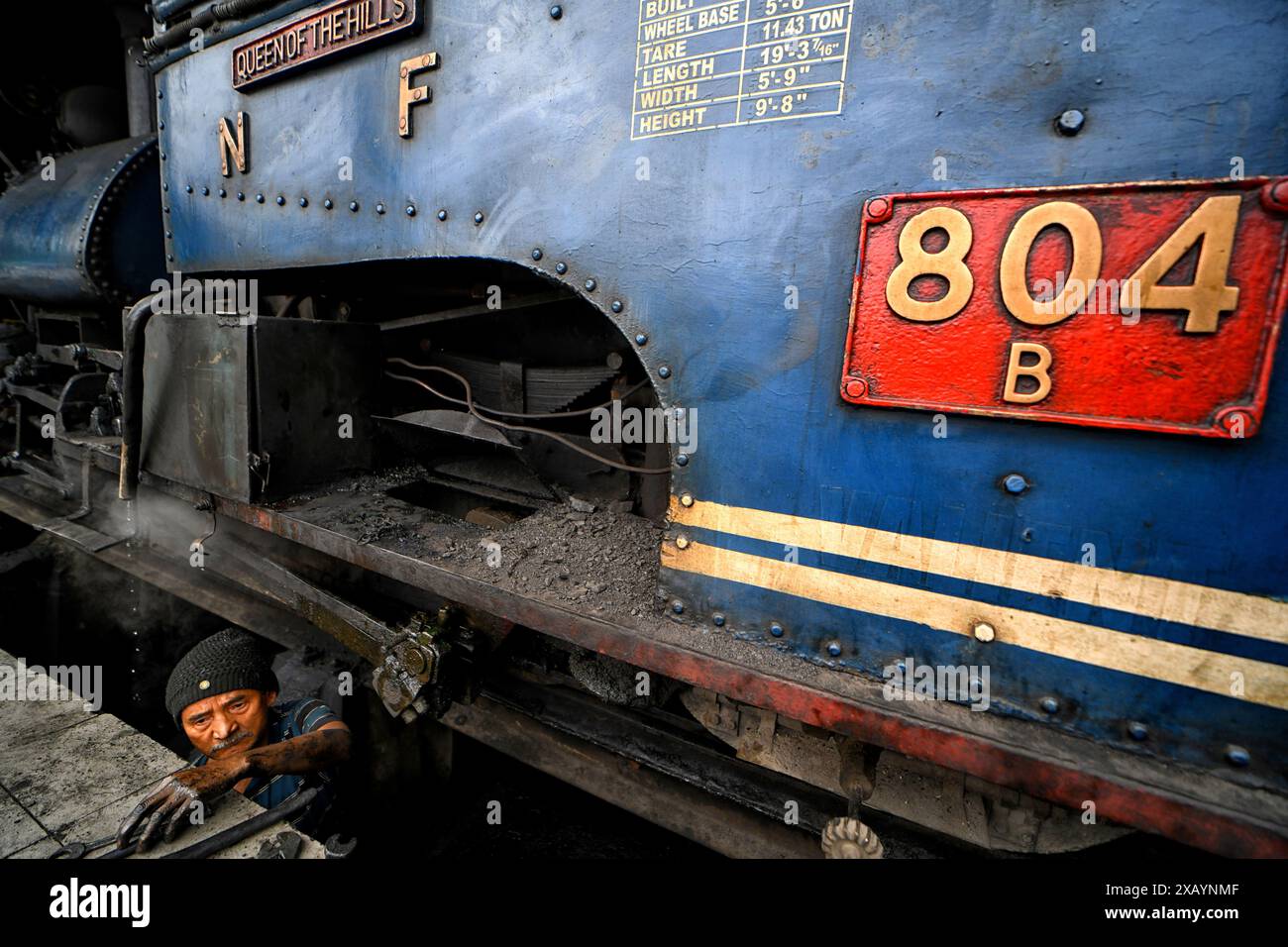 Un dipendente della ferrovia controlla un motore a vapore alla stazione ferroviaria di Darjeeling. La Darjeeling Himalayan Railway, nota anche come "Toy Train", è un treno ferroviario a scartamento ridotto costruito tra il 1879 e il 1881. La ferrovia si sposta fino a un livello di altitudine di 2.200 metri (7.218 piedi). Quattro moderne locomotive diesel gestiscono la maggior parte dei servizi di linea; tuttavia i treni turistici giornalieri da Darjeeling a Ghum (la stazione ferroviaria più alta dell'India) sono gestiti dalle locomotive a vapore vintage di costruzione britannica classe B. Il DHR è stato dichiarato patrimonio dell'umanità dall'UNESCO nel 1999. Foto Stock